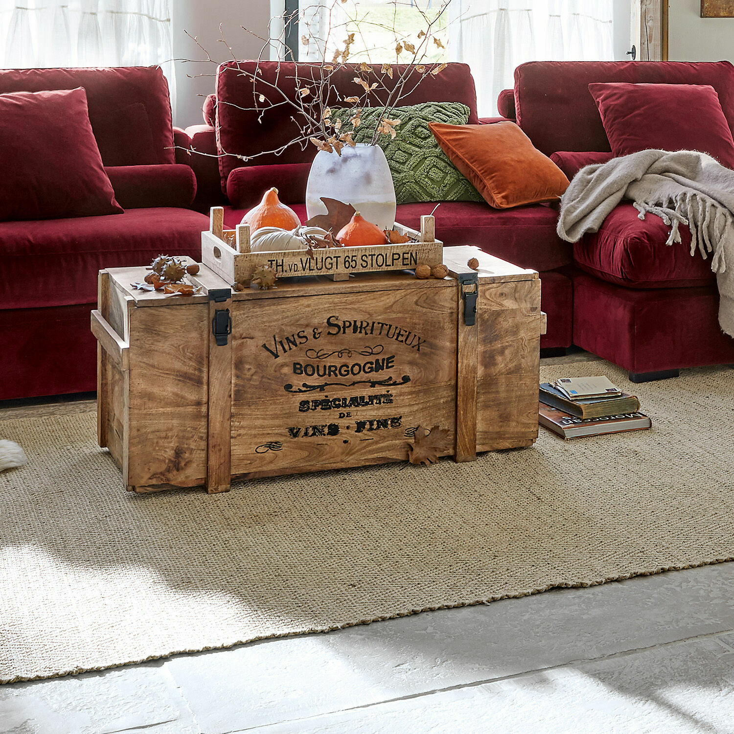 Caisse en bois Eskeny Coffre en bois avec inscription sur tapis devant un canapé bordeaux avec coussins et plaid dans un salon
