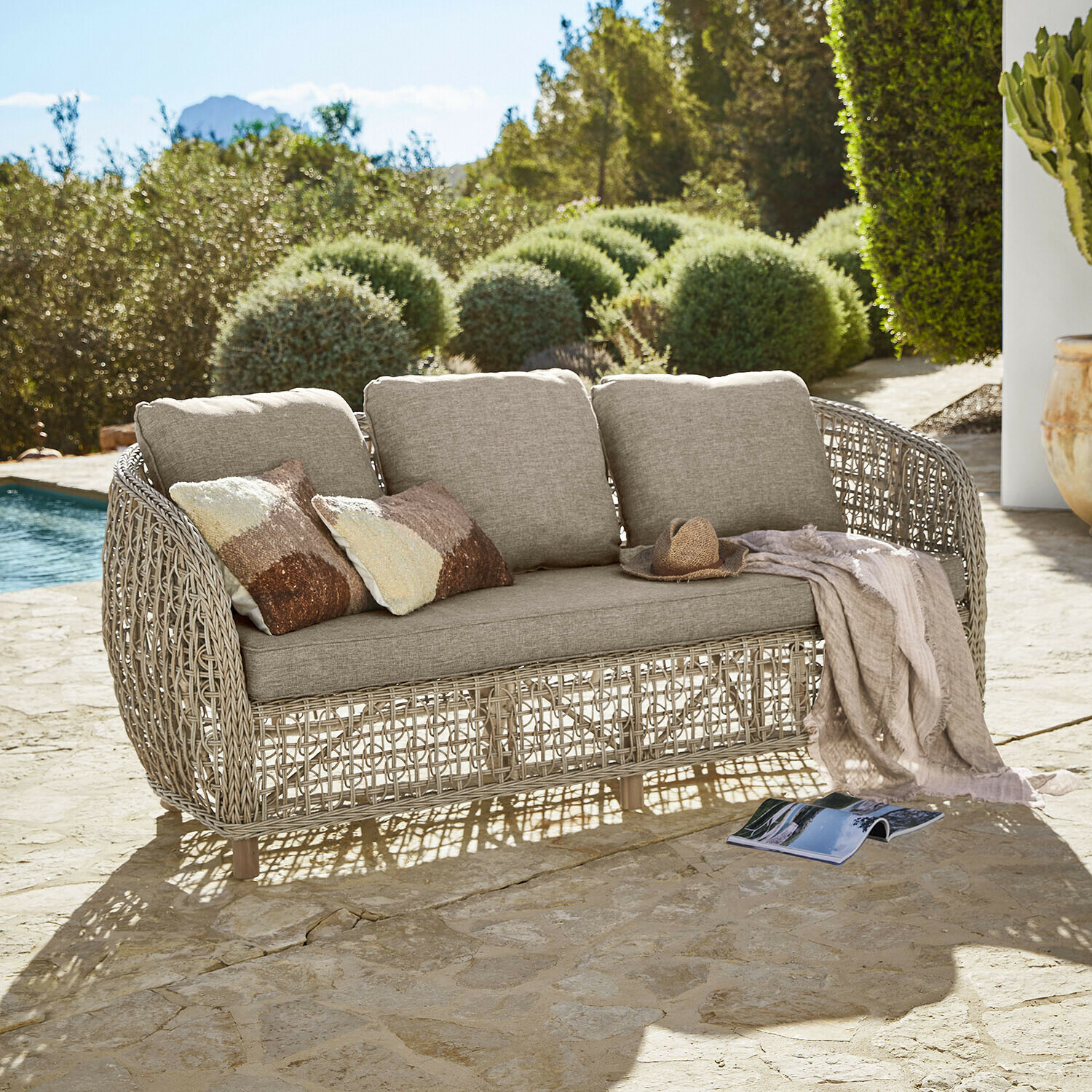 Canapé Ventiglio Canapé d'extérieur beige avec coussins et structure en rotin tressé sur terrasse en pierre près de la piscine