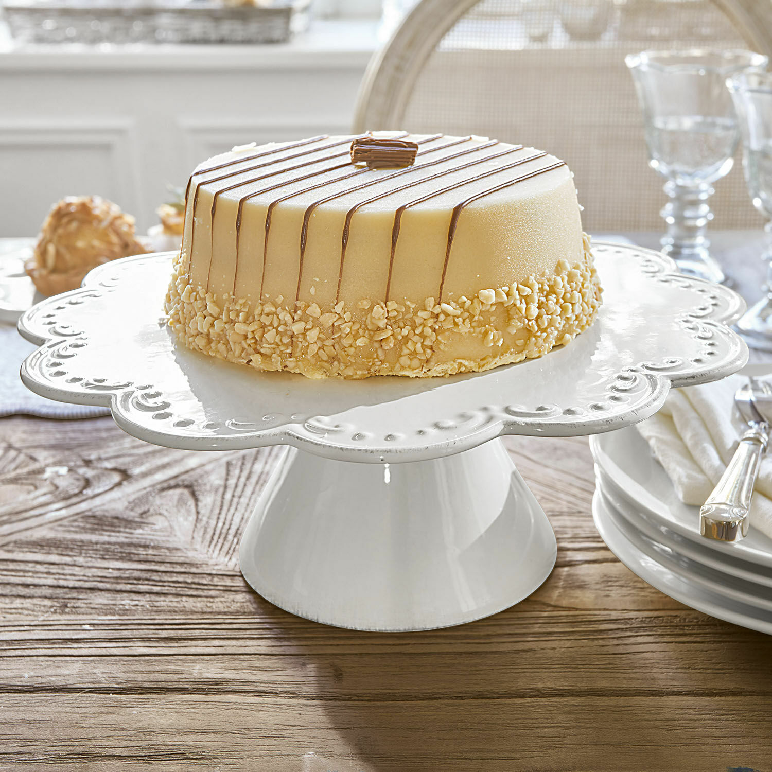Présentoir à gâteau en céramique blanche avec bord décoratif sur table en bois dans une salle à manger