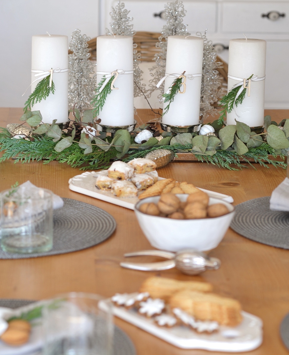 Bougies blanches d'avent avec branches vertes et chiffres en bois sur plateau en bois avec biscuits sur table