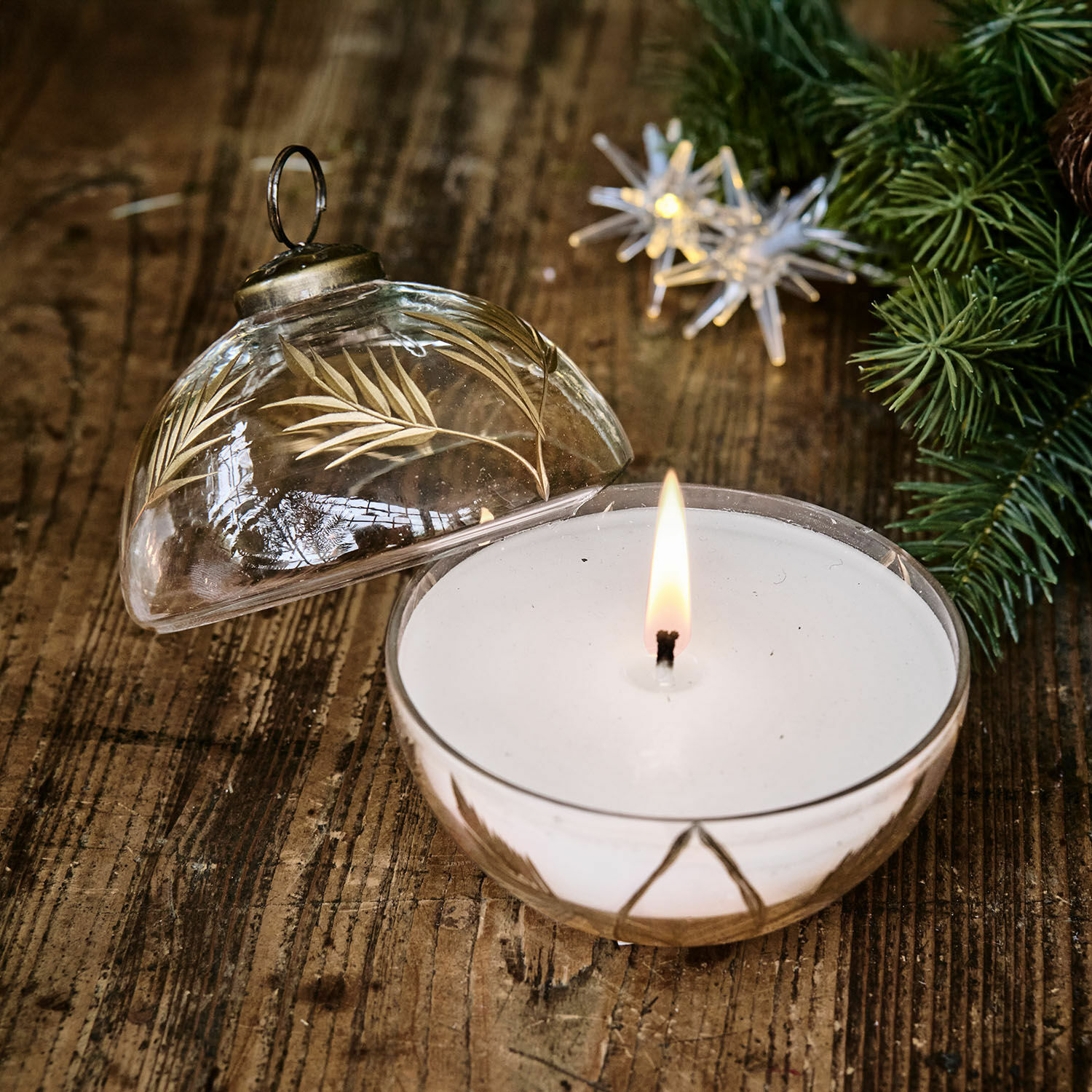 Bougie parfumée dans un récipient en verre transparent avec motif doré de feuilles sur une table en bois