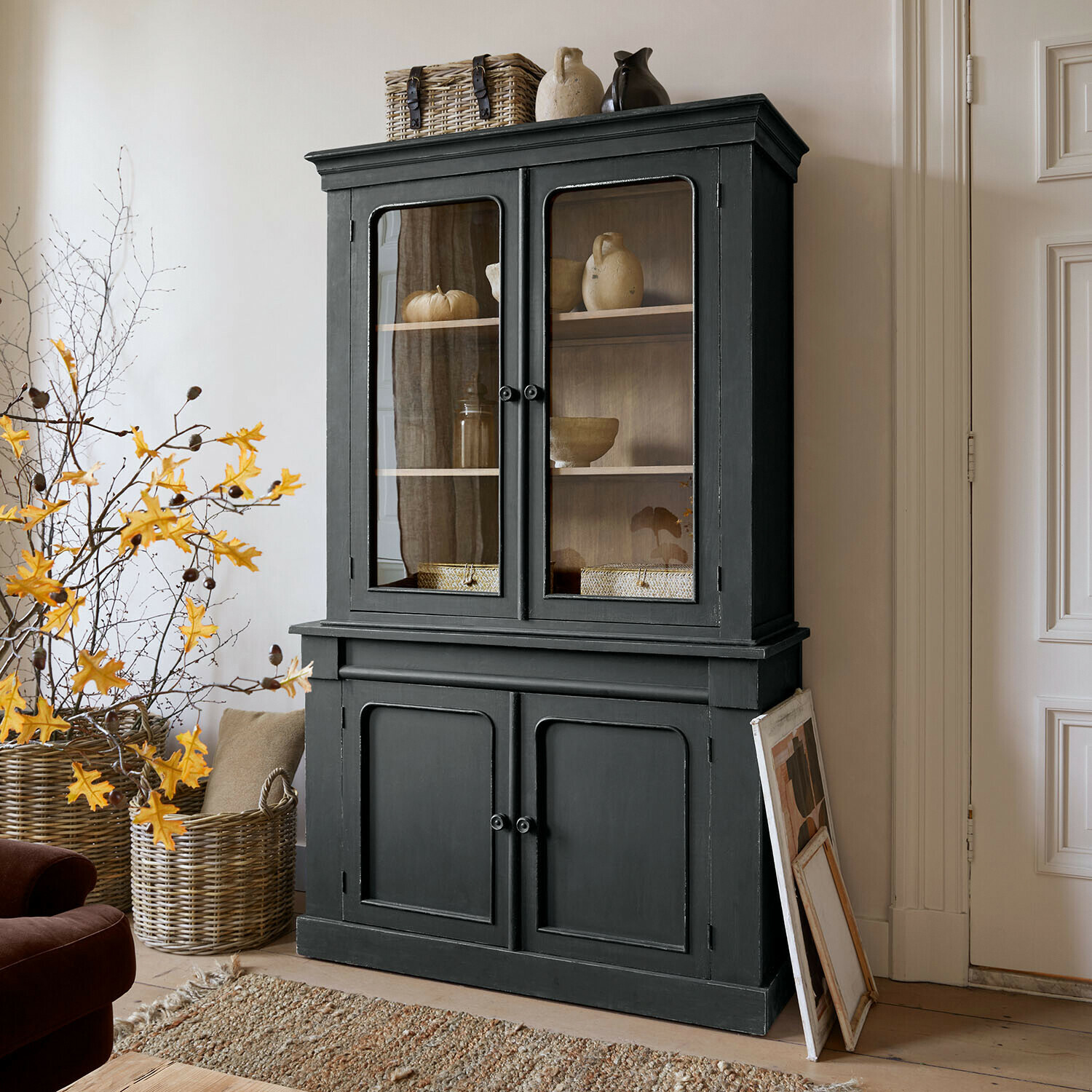 Vaisselier Aldwyn Vitrine en bois noir avec portes vitrées et décorations en céramique dans un salon lumineux