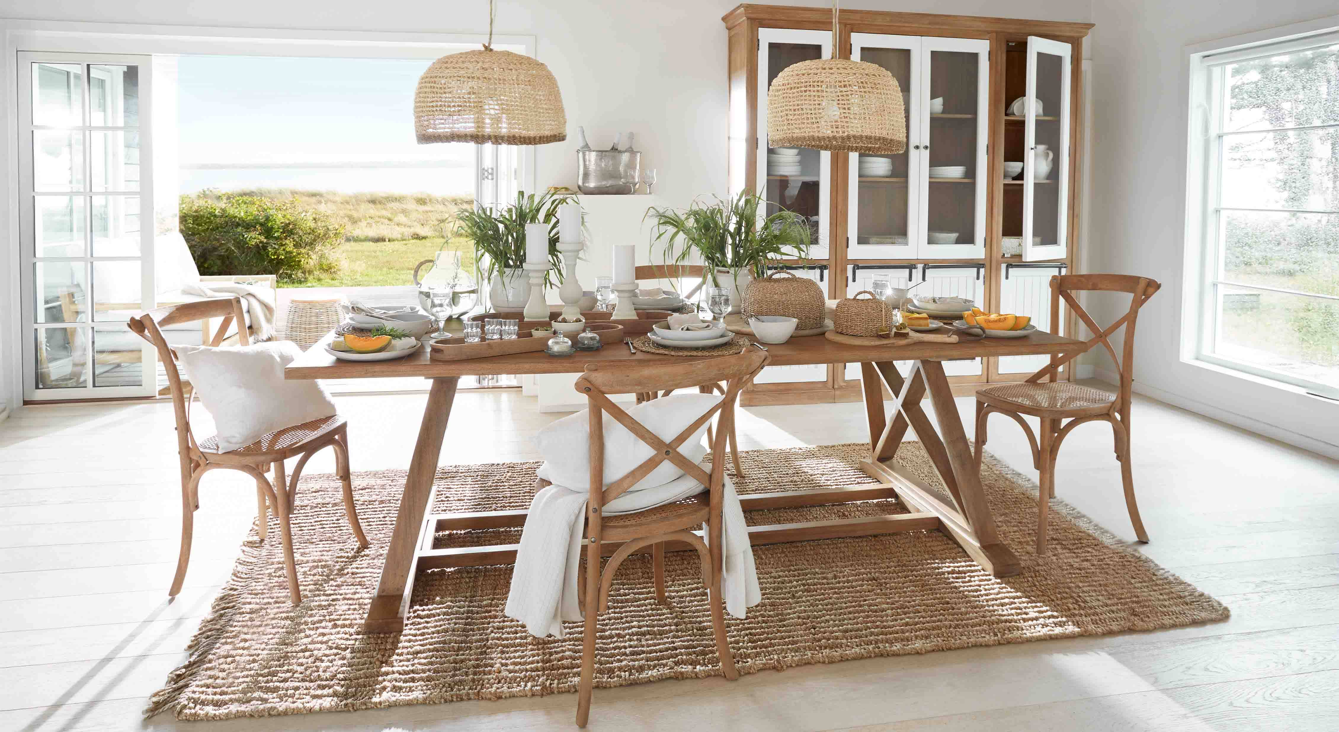 Salle à manger avec table en bois et chaises en rotin sur tapis naturel, décorations végétales et suspensions en osier