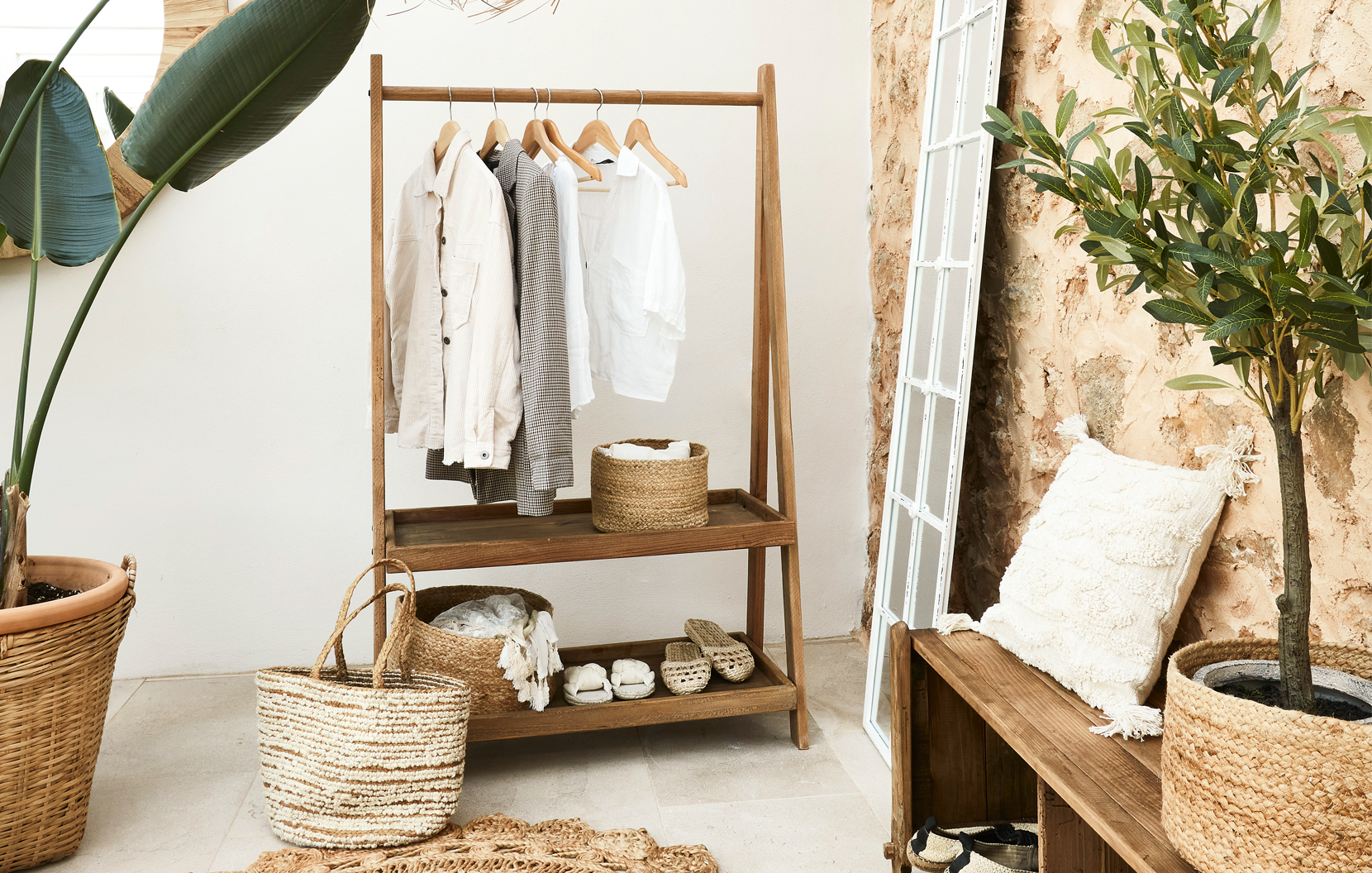 Porte-vêtements en bois avec chemises claires et paniers en osier dans un intérieur bohème