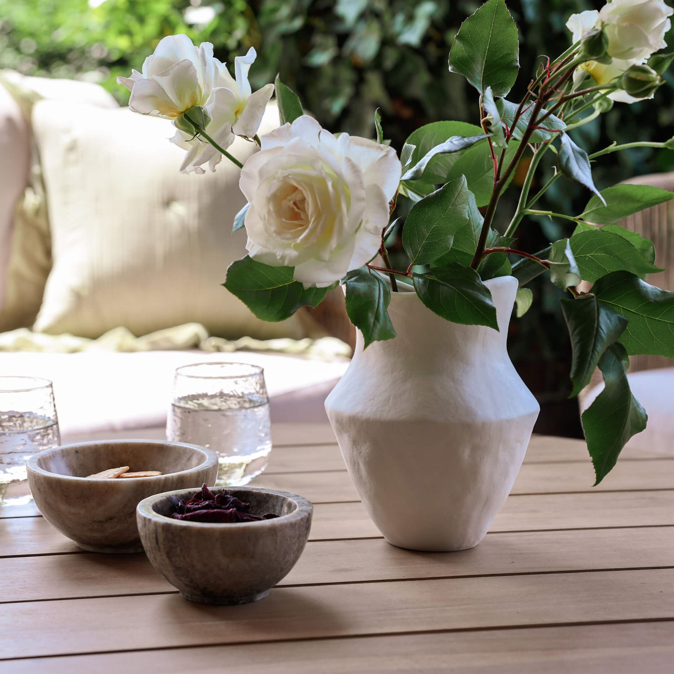 Vase en céramique blanche avec roses blanches sur table en bois avec bols et verres d'eau