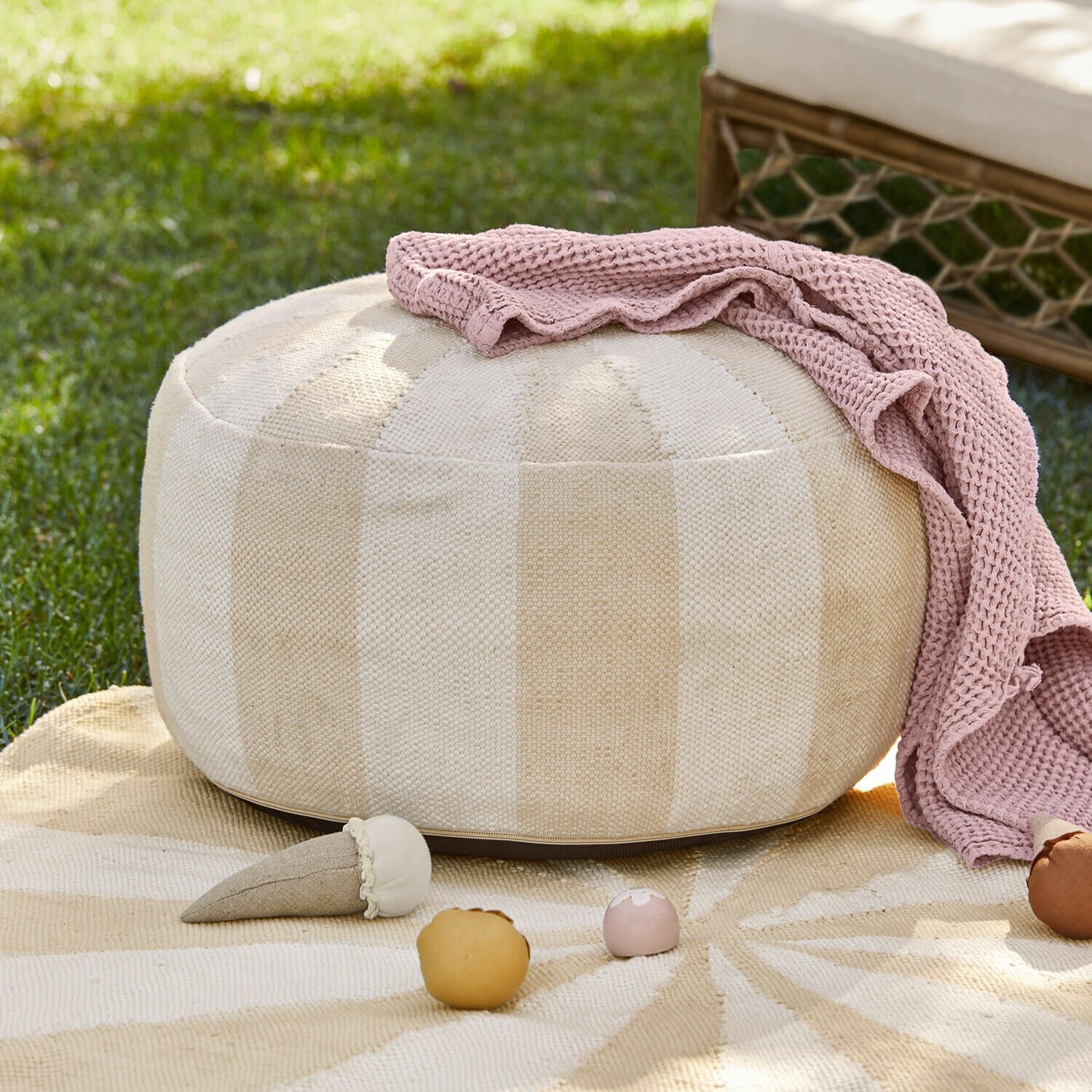 Pouf rond beige en tissu avec couverture tricotée rose et jouets sur l'herbe en extérieur
