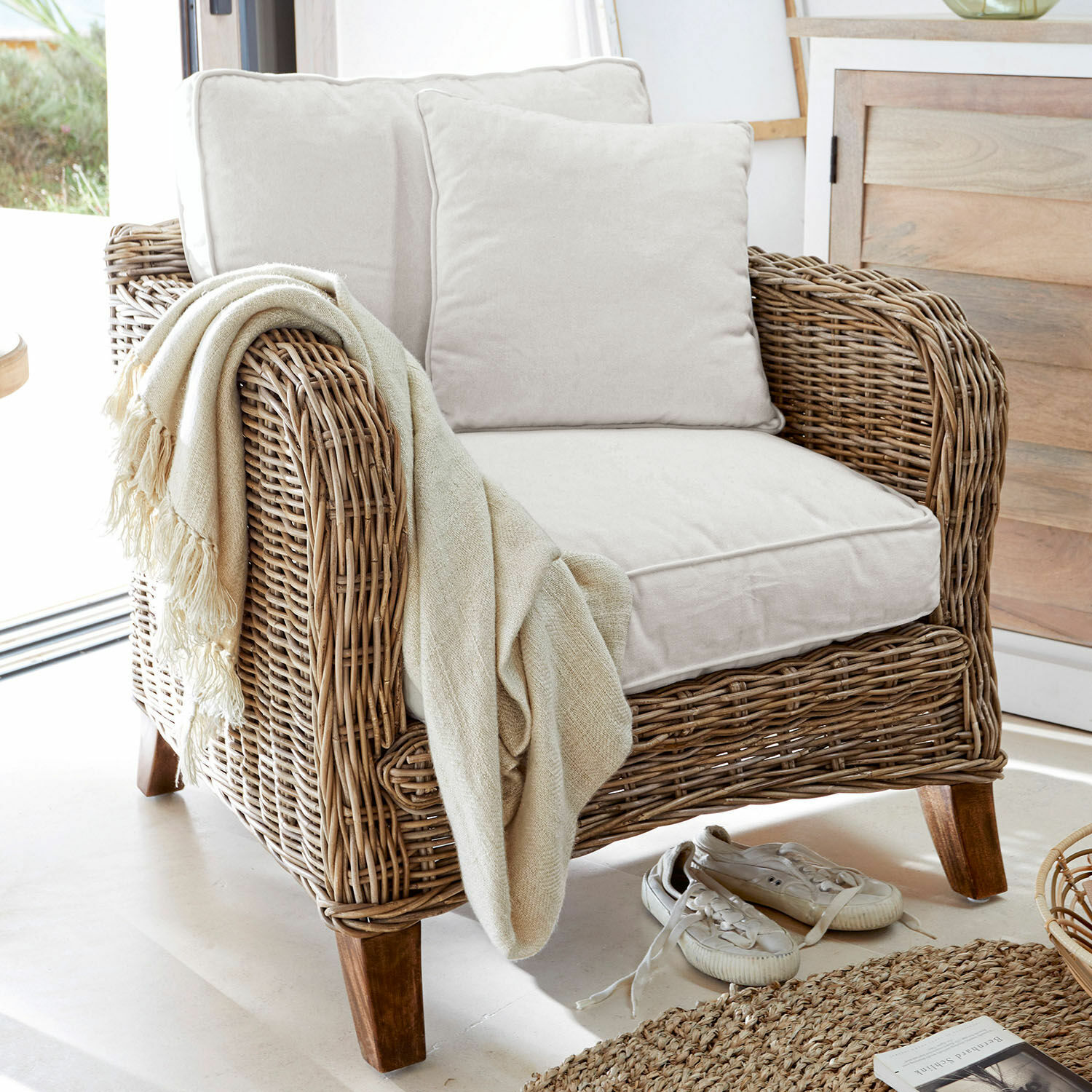 Fauteuil Colroy Fauteuil en rotin avec coussins crème et plaid beige, ambiance naturelle, mobilier en rotin
