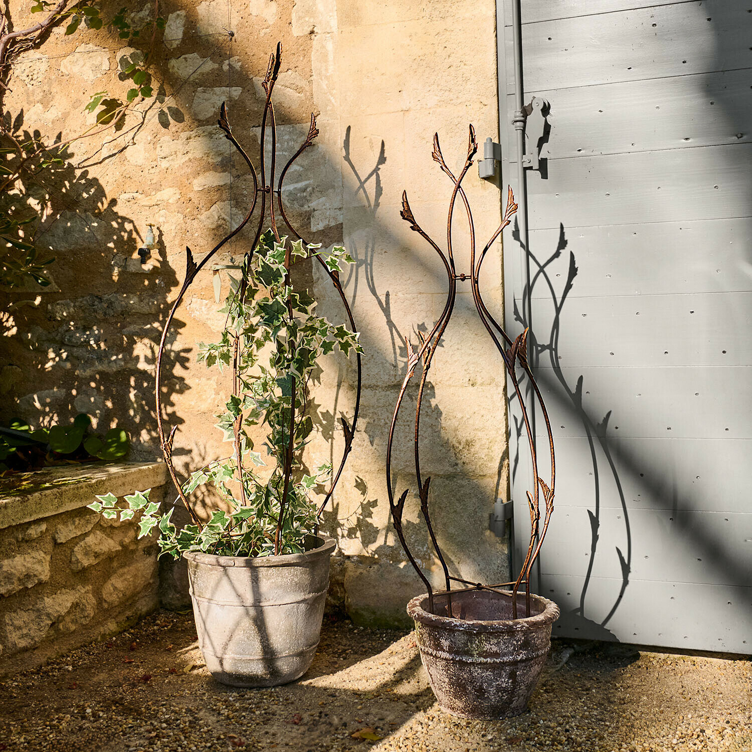 Deux supports métalliques décoratifs pour plantes en pots en pierre sur une terrasse ensoleillée