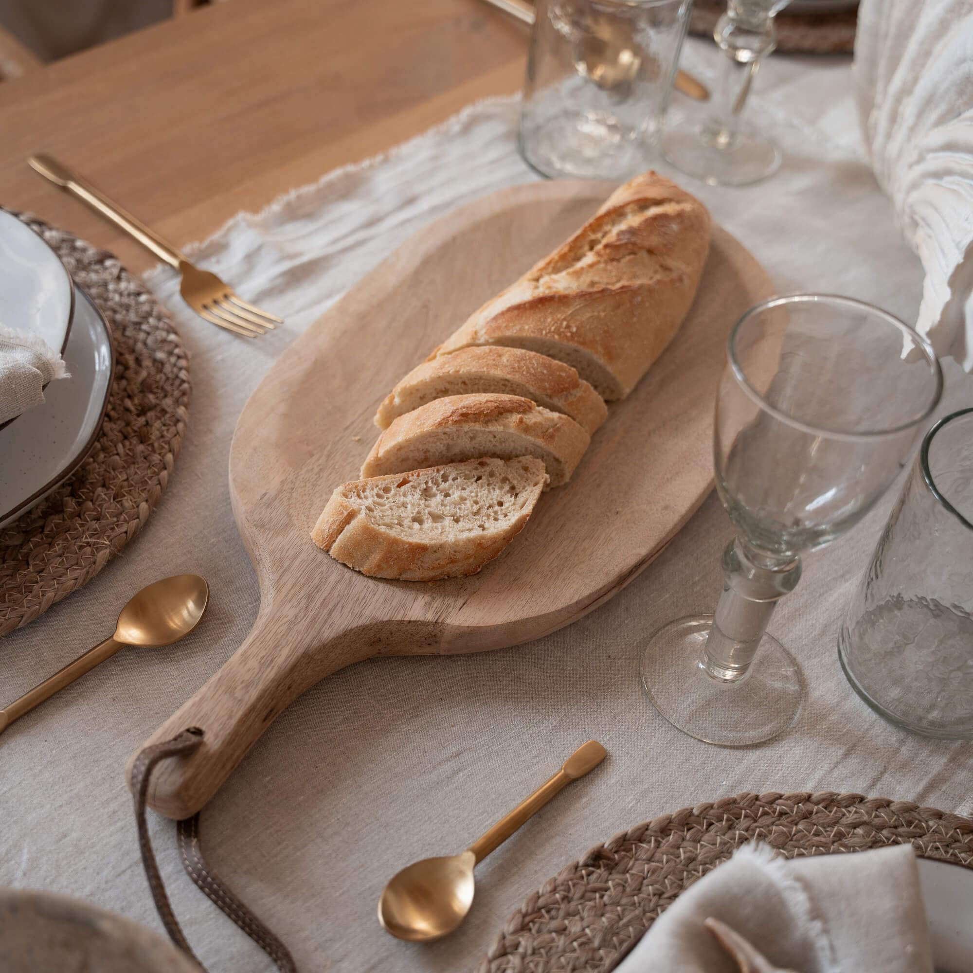 Planche à découper en bois avec baguette tranchée sur table avec vaisselle et couverts dorés