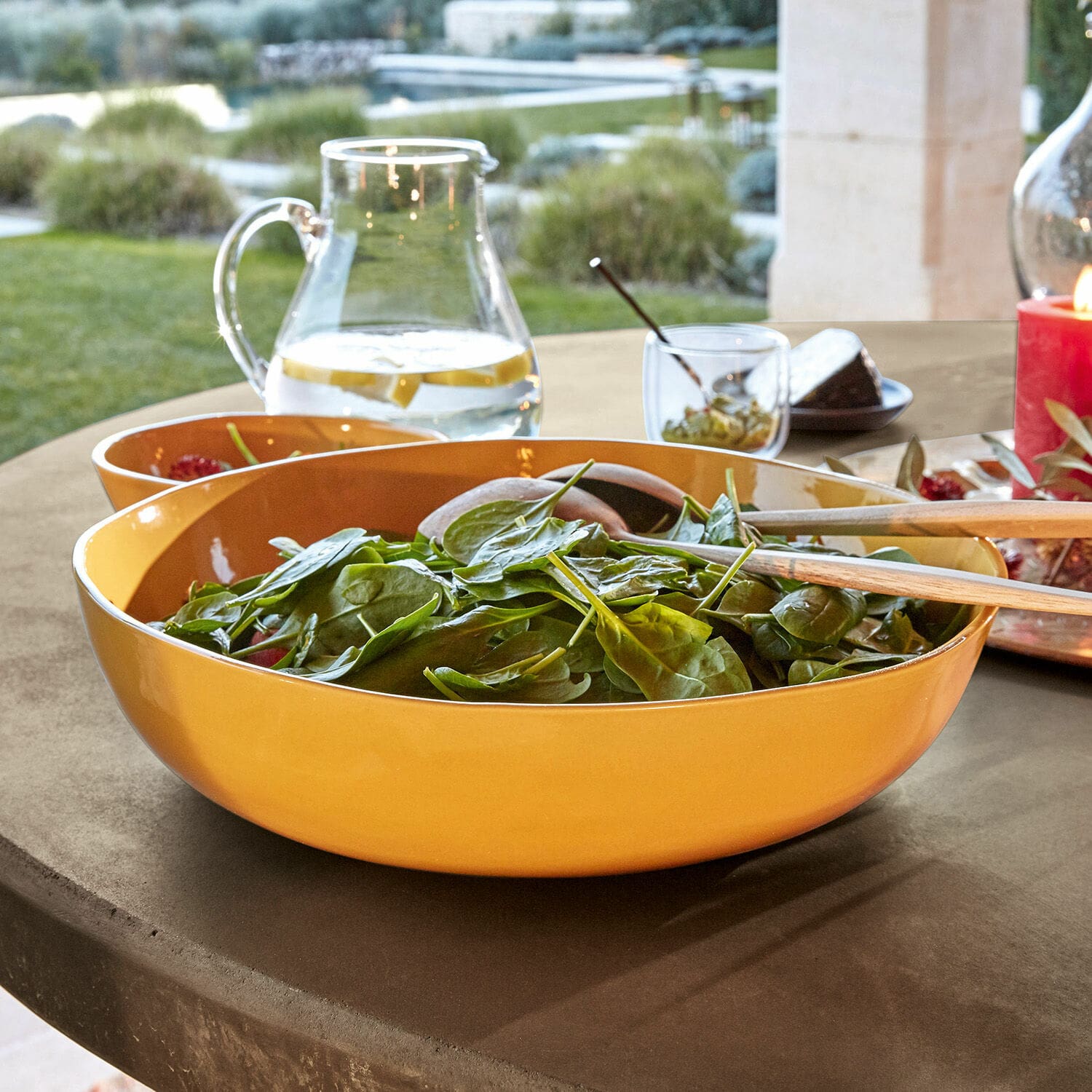 Saladier en céramique jaune avec couverts en bois sur une table extérieure
