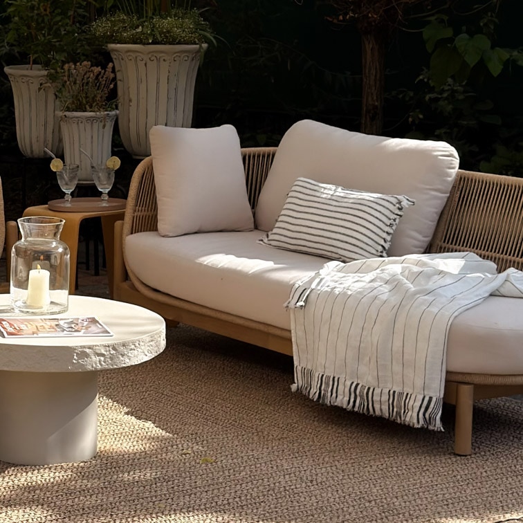 Canapé d'extérieur moderne avec coussins clairs et plaid rayé sur tapis naturel dans un jardin