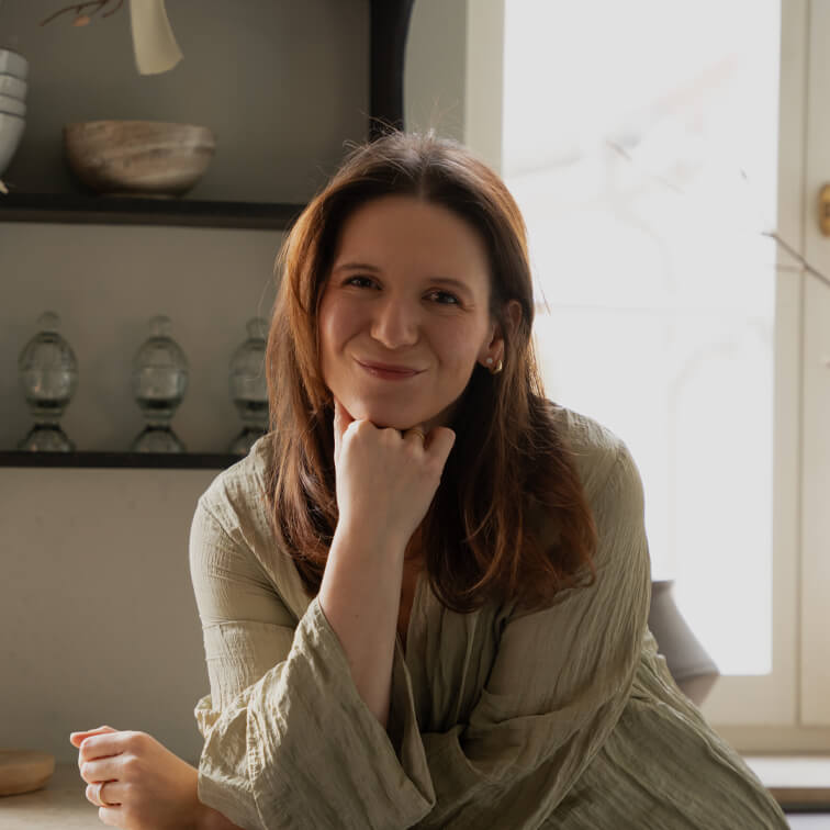 Femme souriante en chemise verte en lin assise à une table dans un intérieur lumineux