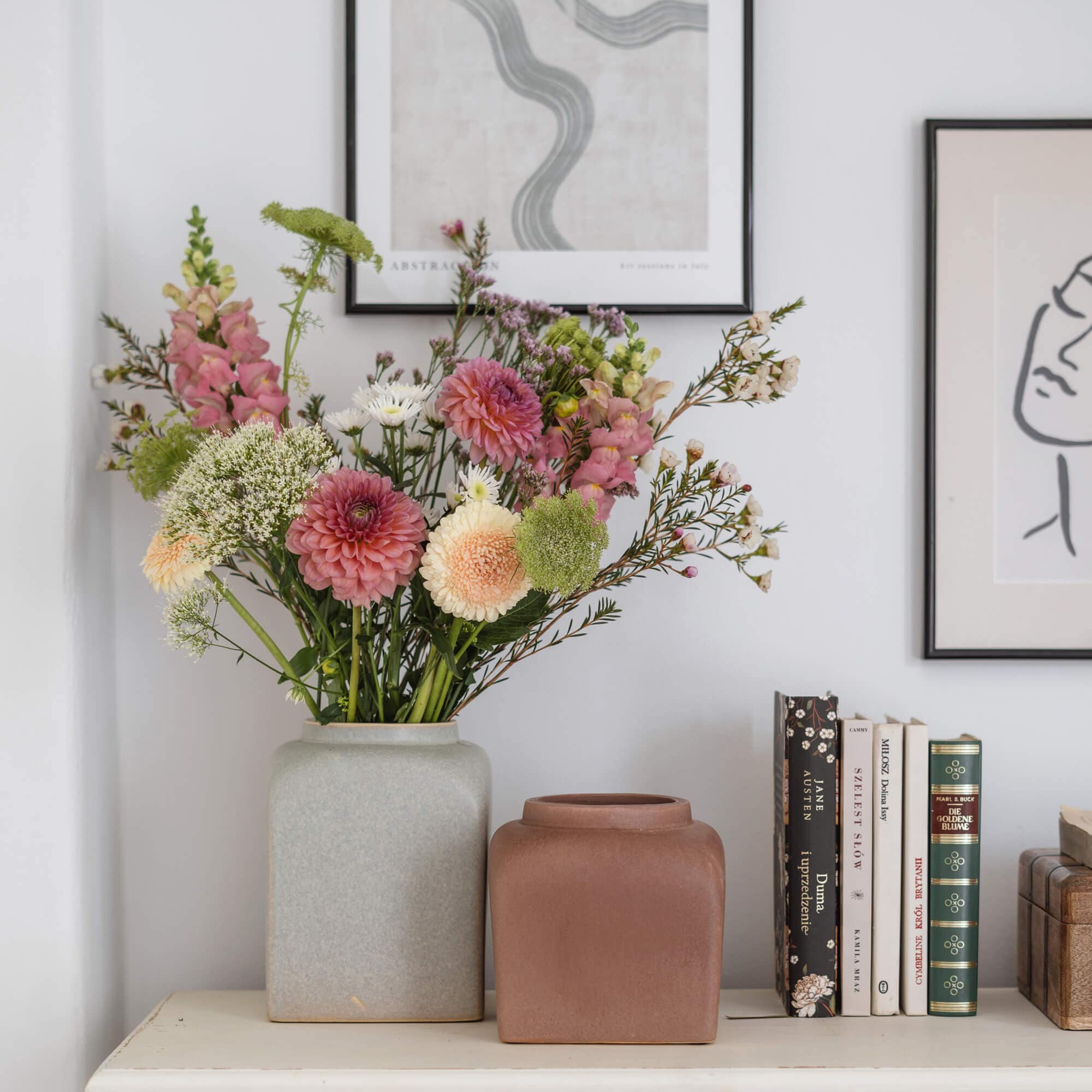 Deux vases en céramique gris et marron sur une table blanche avec bouquet de fleurs et livres