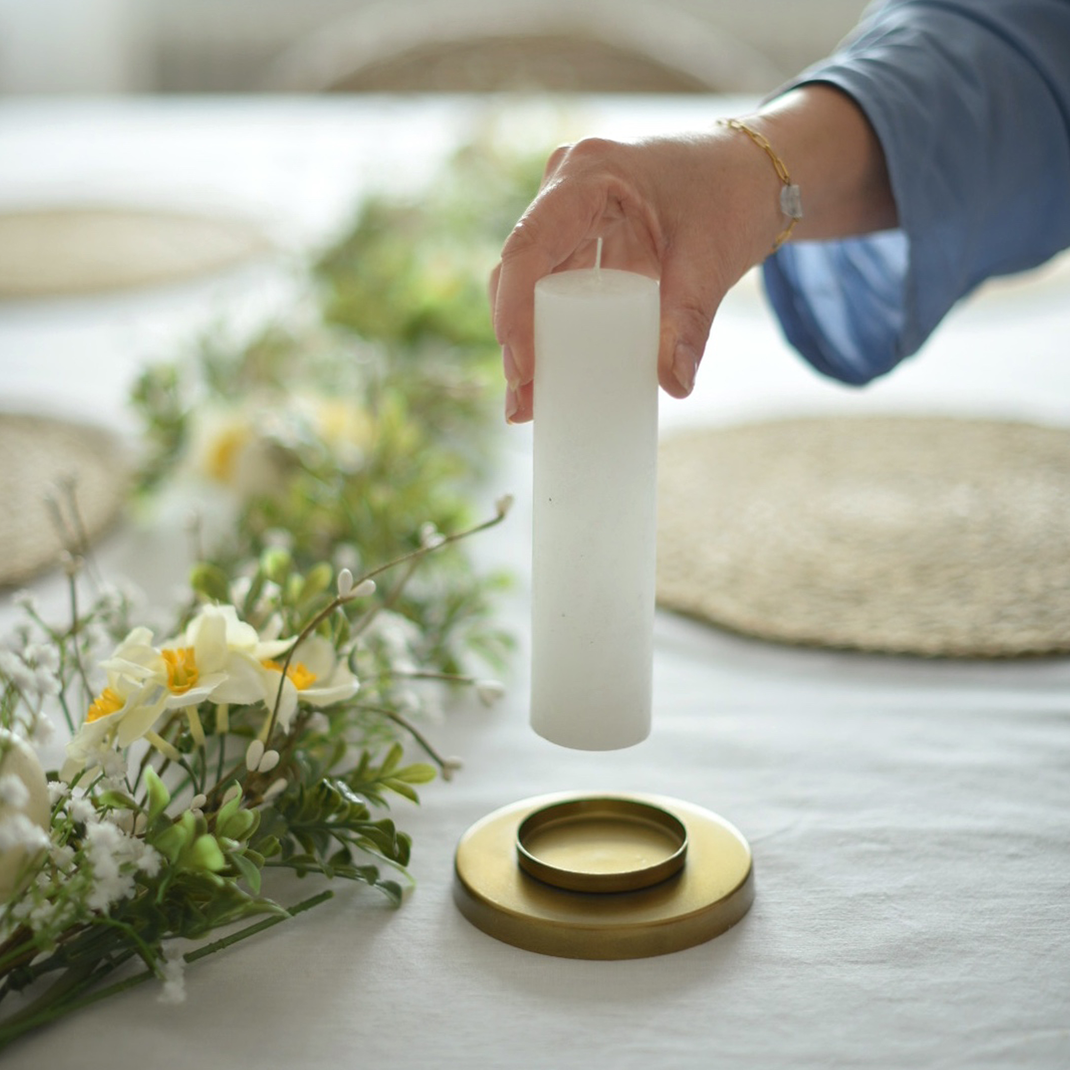 Bougie blanche cylindrique tenue au-dessus d'un chandelier doré avec décoration florale sur une nappe blanche