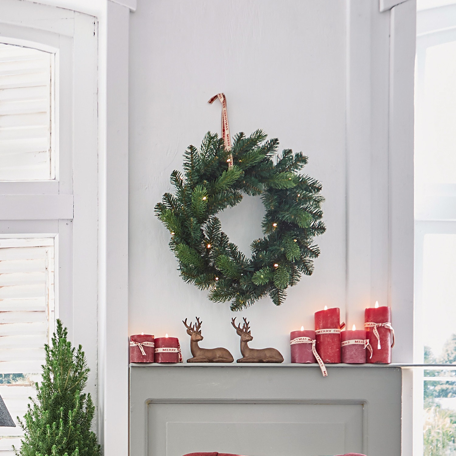 Couronne LED Regin Couronne de Noël verte avec lumières LED et bougies rouges sur une cheminée grise décorée de rennes