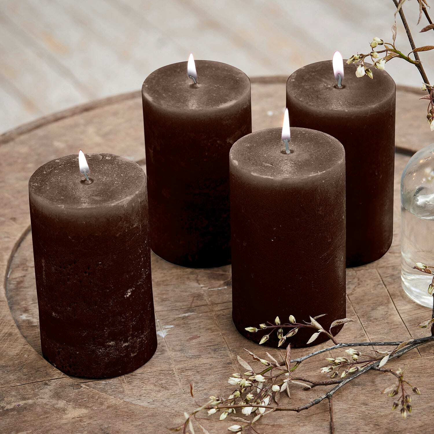 Lot de 4 bougies Braga Quatre bougies brunes en cire allumées sur une table en bois avec des branches décoratives