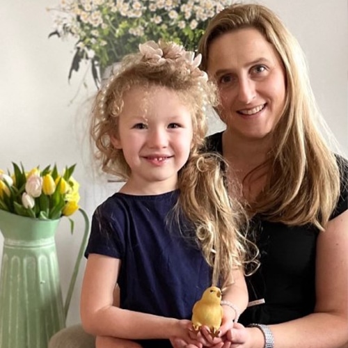 Femme souriante et petite fille aux cheveux blonds tenant une décoration oiseau jaune dans un intérieur lumineux