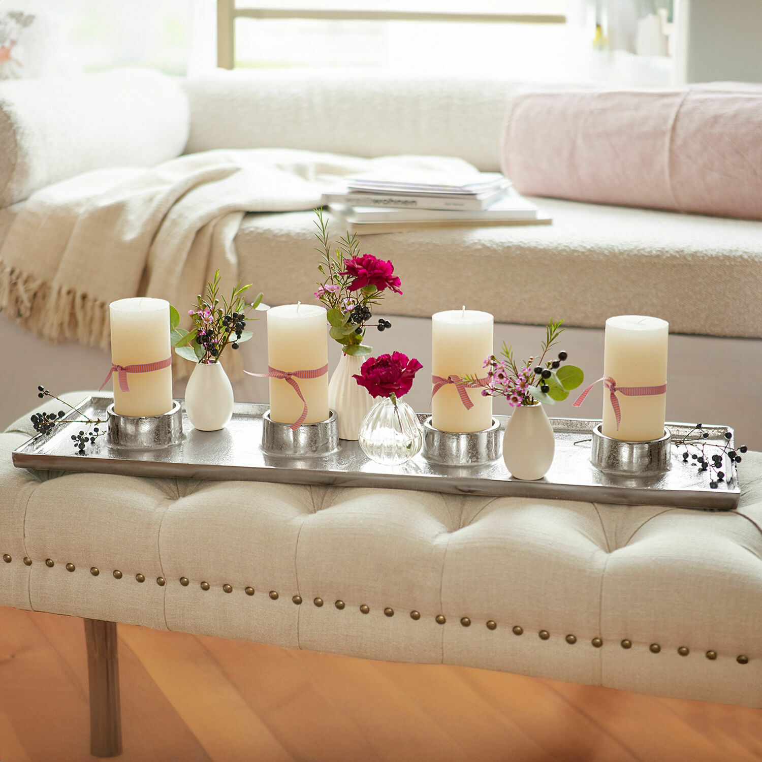 Bougeoir Mareuil Plateau en métal avec quatre bougies crème et petits vases fleuris sur un banc beige