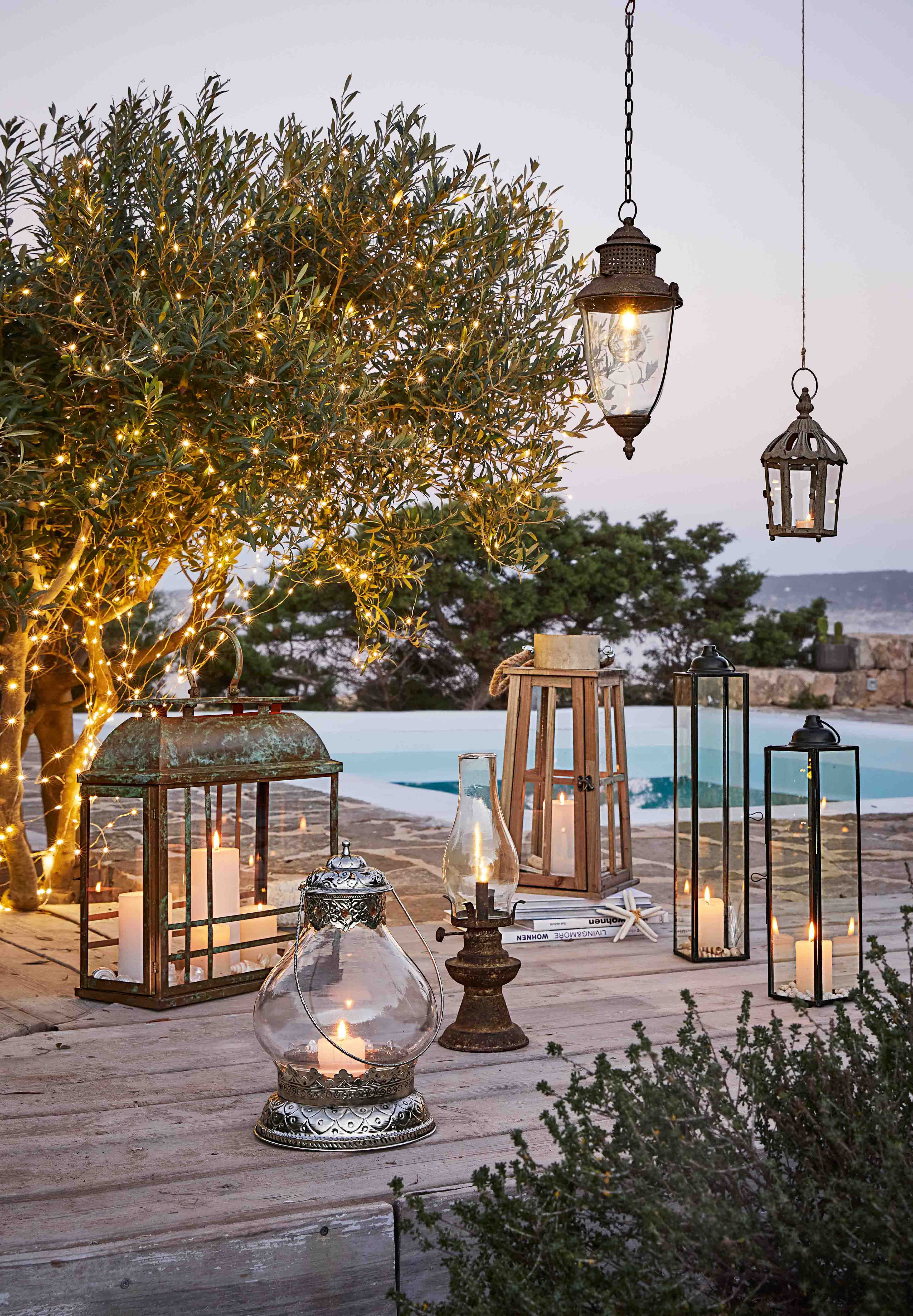 Ensemble de lanternes et bougies sur terrasse en bois avec arbre décoré de guirlandes lumineuses LED