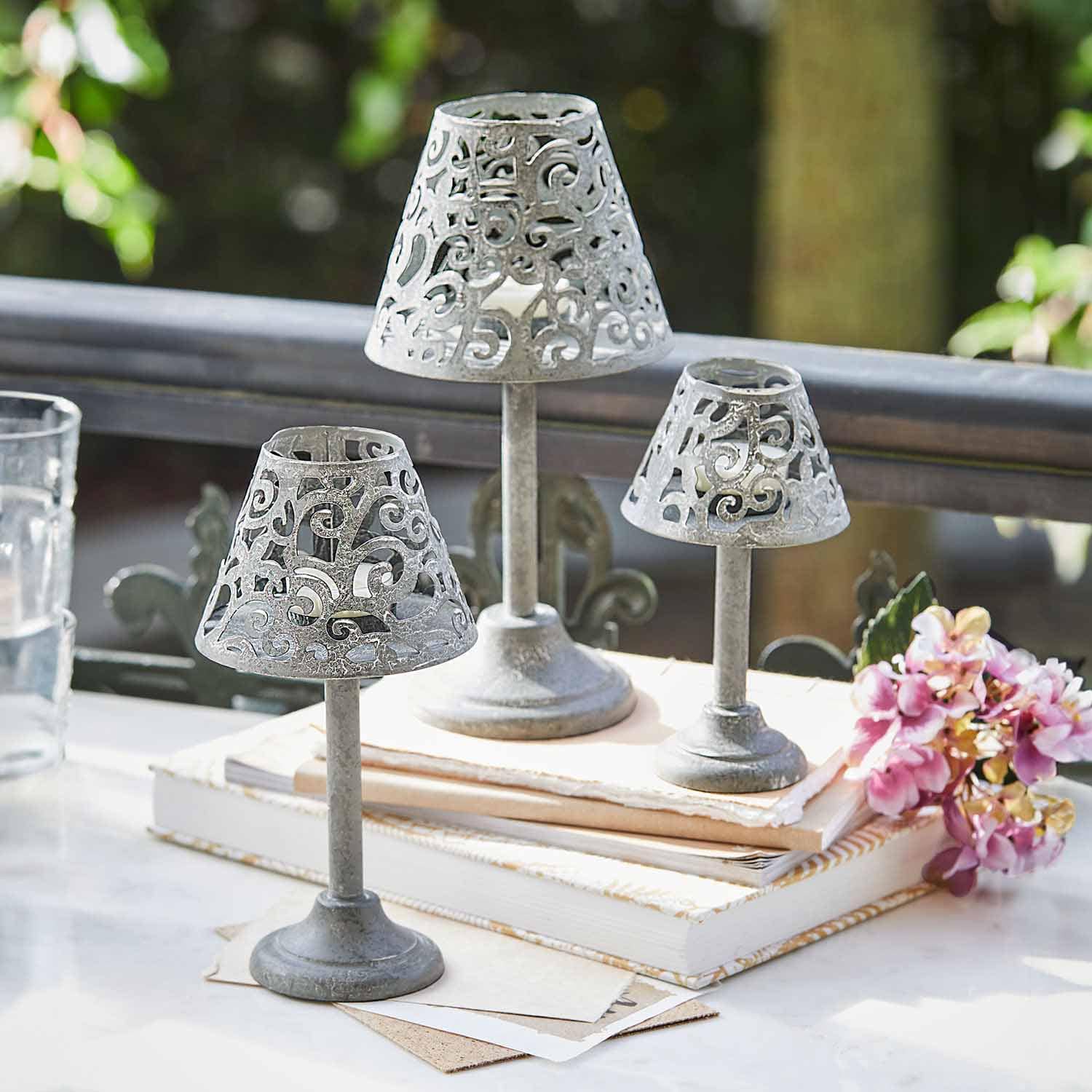 Ensemble de trois bougeoirs en métal gris avec motif ajouré posés sur des livres sur une table
