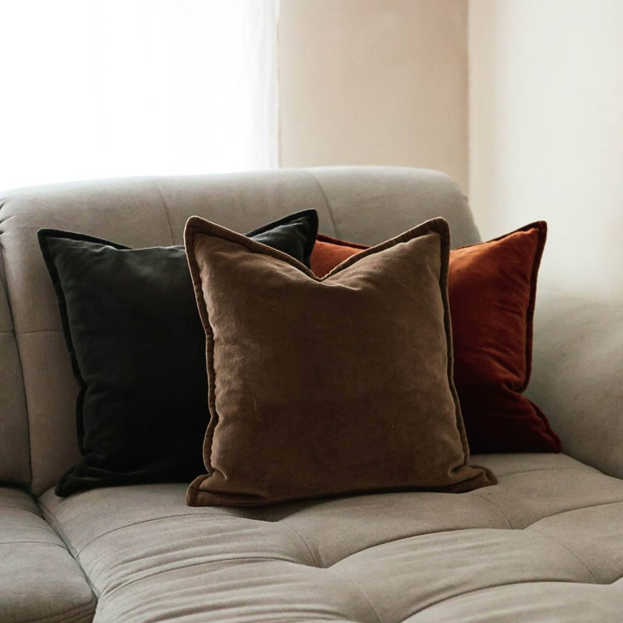 Trois coussins décoratifs doux en noir, marron et brique sur un canapé gris clair