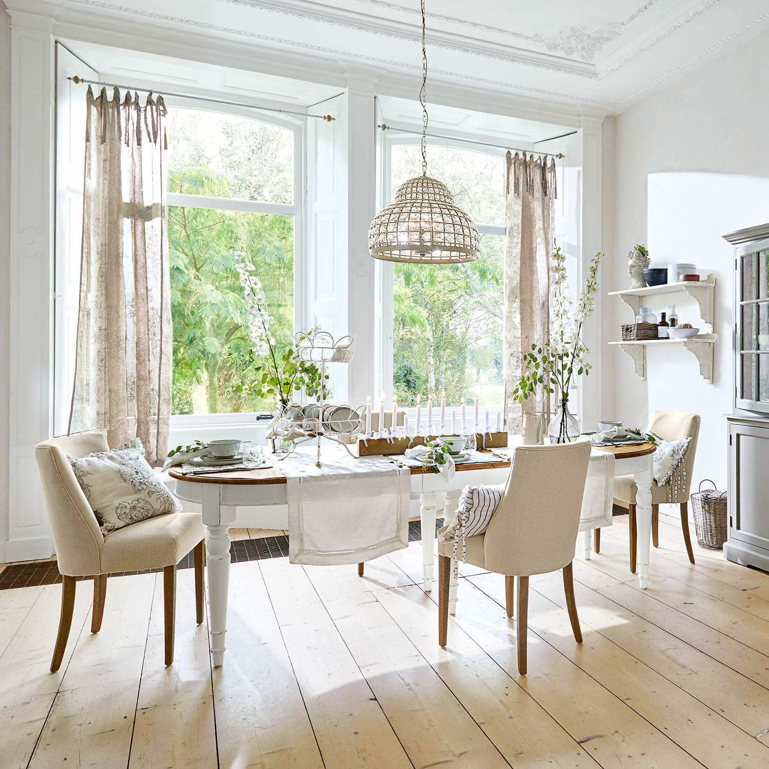 Table Pinecrest Salle à manger avec table en bois blanc et chaises beige sur parquet clair, décorations et suspension en osier