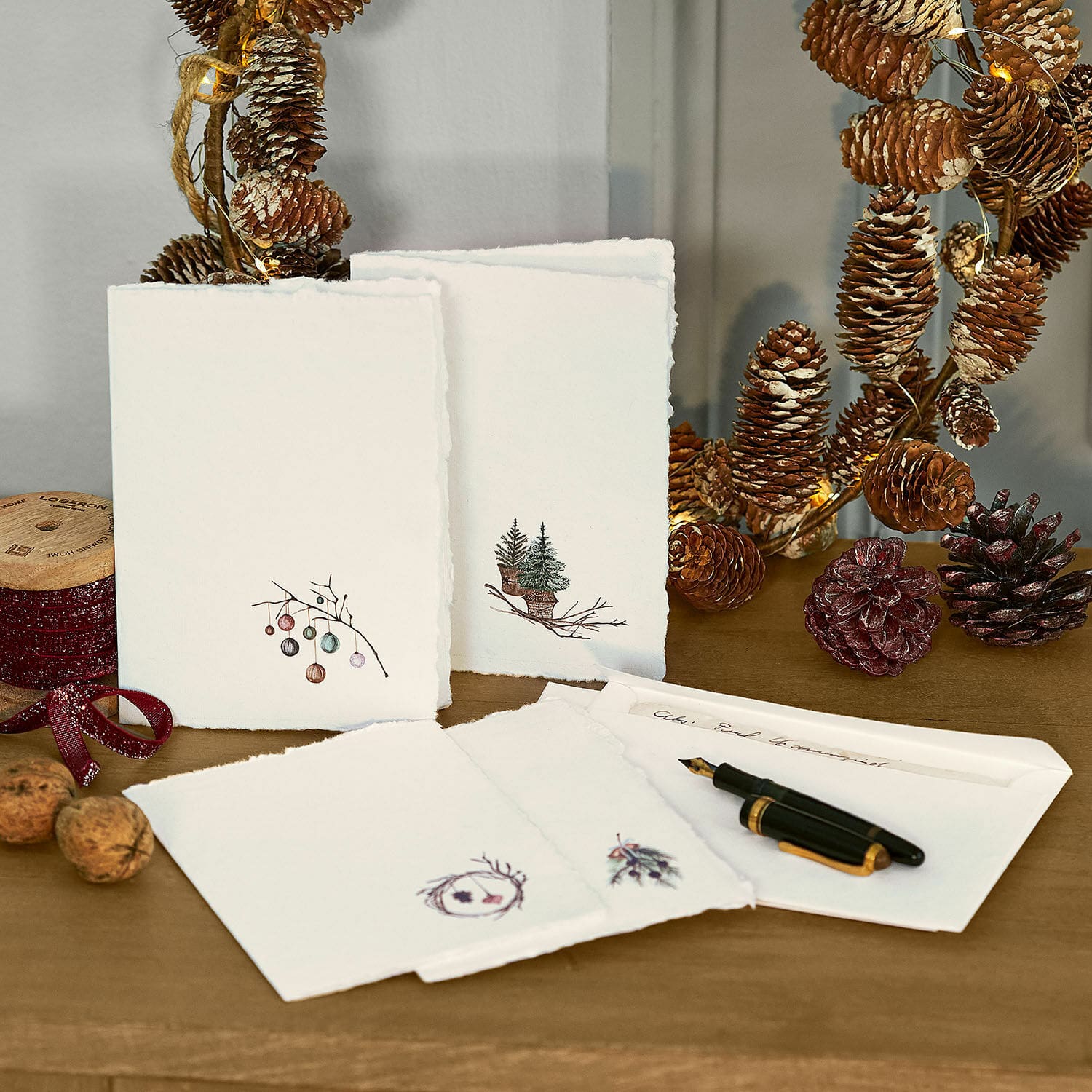 Lot de 4 cartes de vœux Velorine Ensemble de cartes de vœux en papier avec motifs sapins et pommes de pin sur table en bois avec stylo plume et décorations