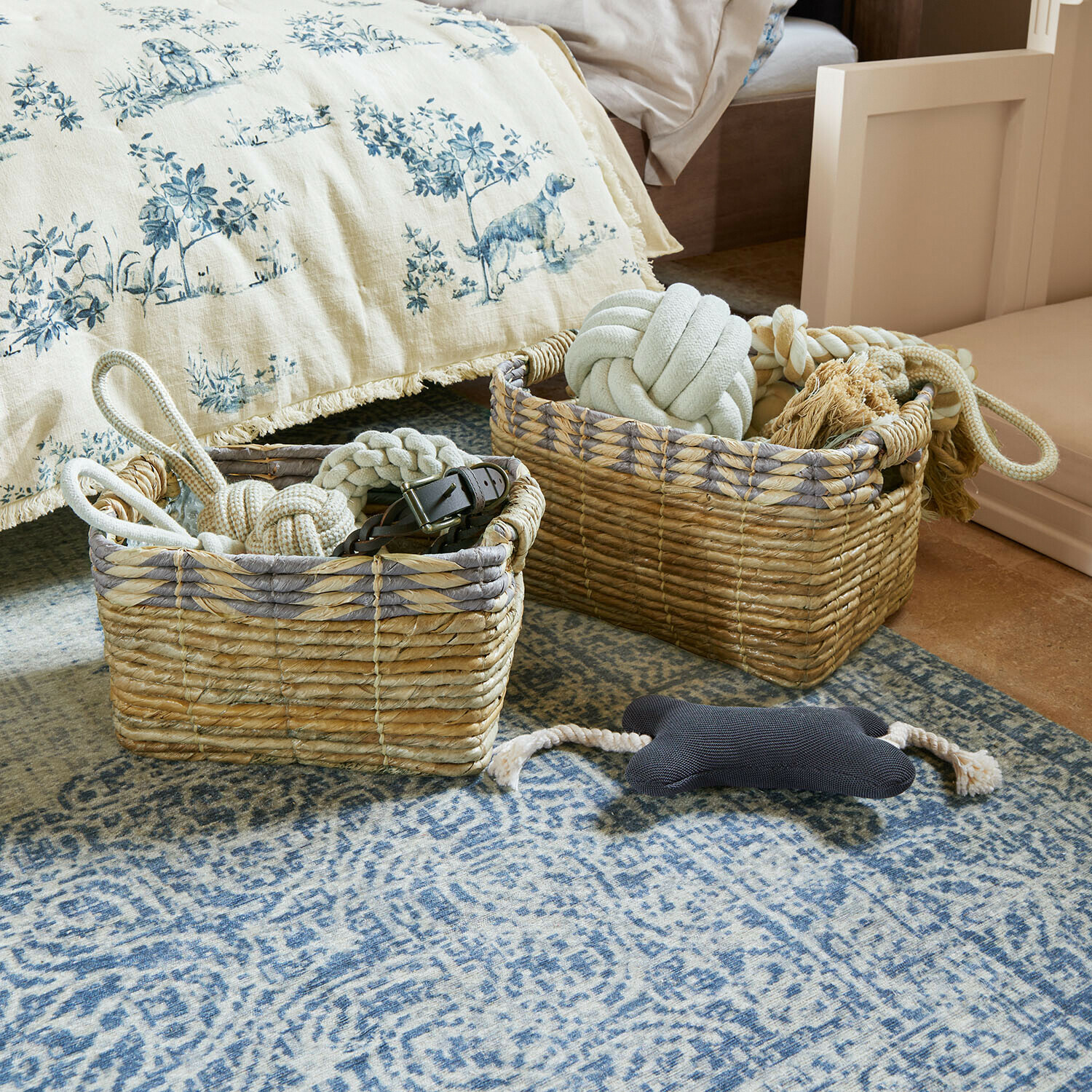 Deux paniers en osier naturel avec jouets pour chiens sur un tapis bleu dans une chambre à coucher