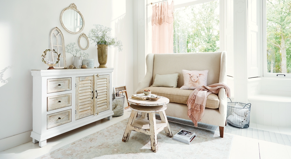 Salon cosy shabby chic avec buffet en bois blanc et canapé beige avec coussins et plaid rose