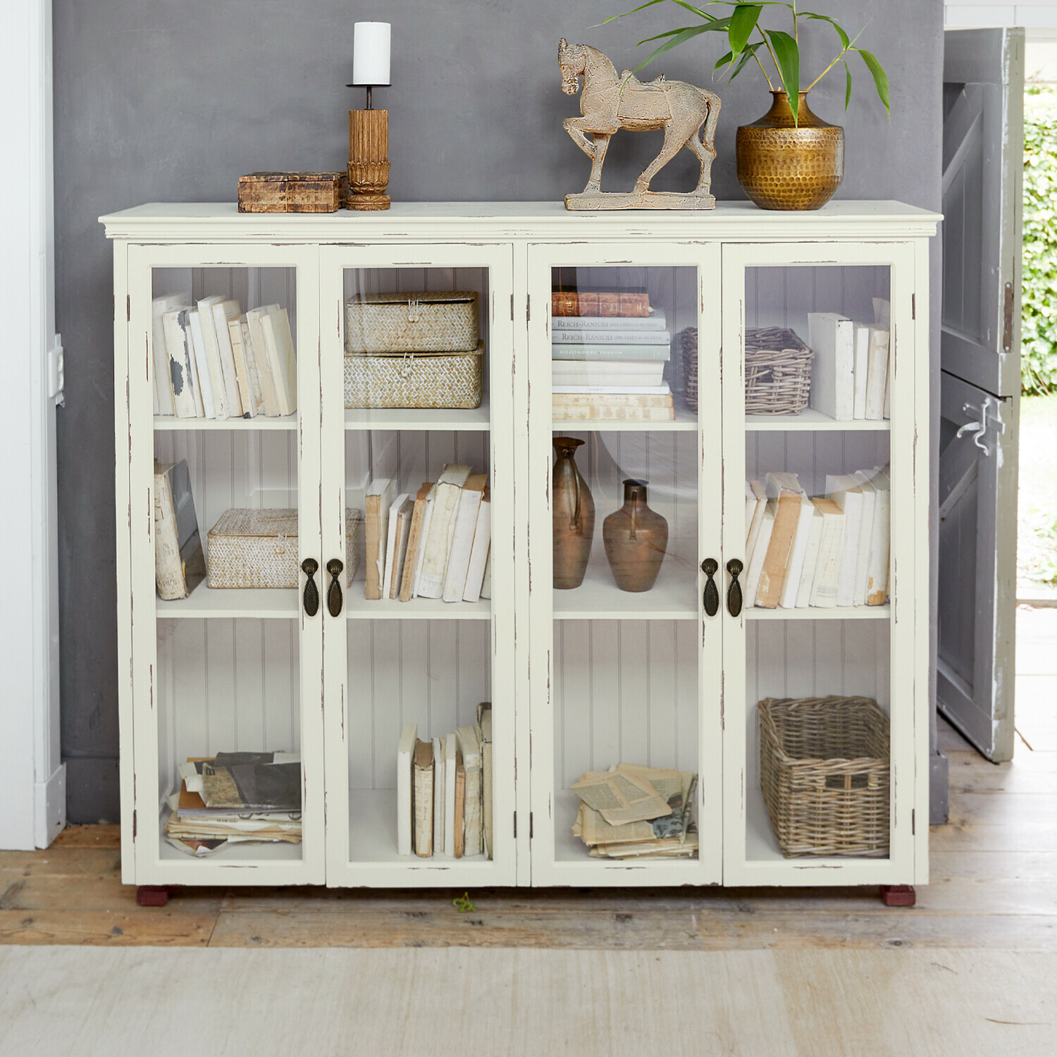 Vitrine Eastbridge Vitrine en bois blanc avec portes vitrées, décorée de livres et objets vintage dans un intérieur cosy