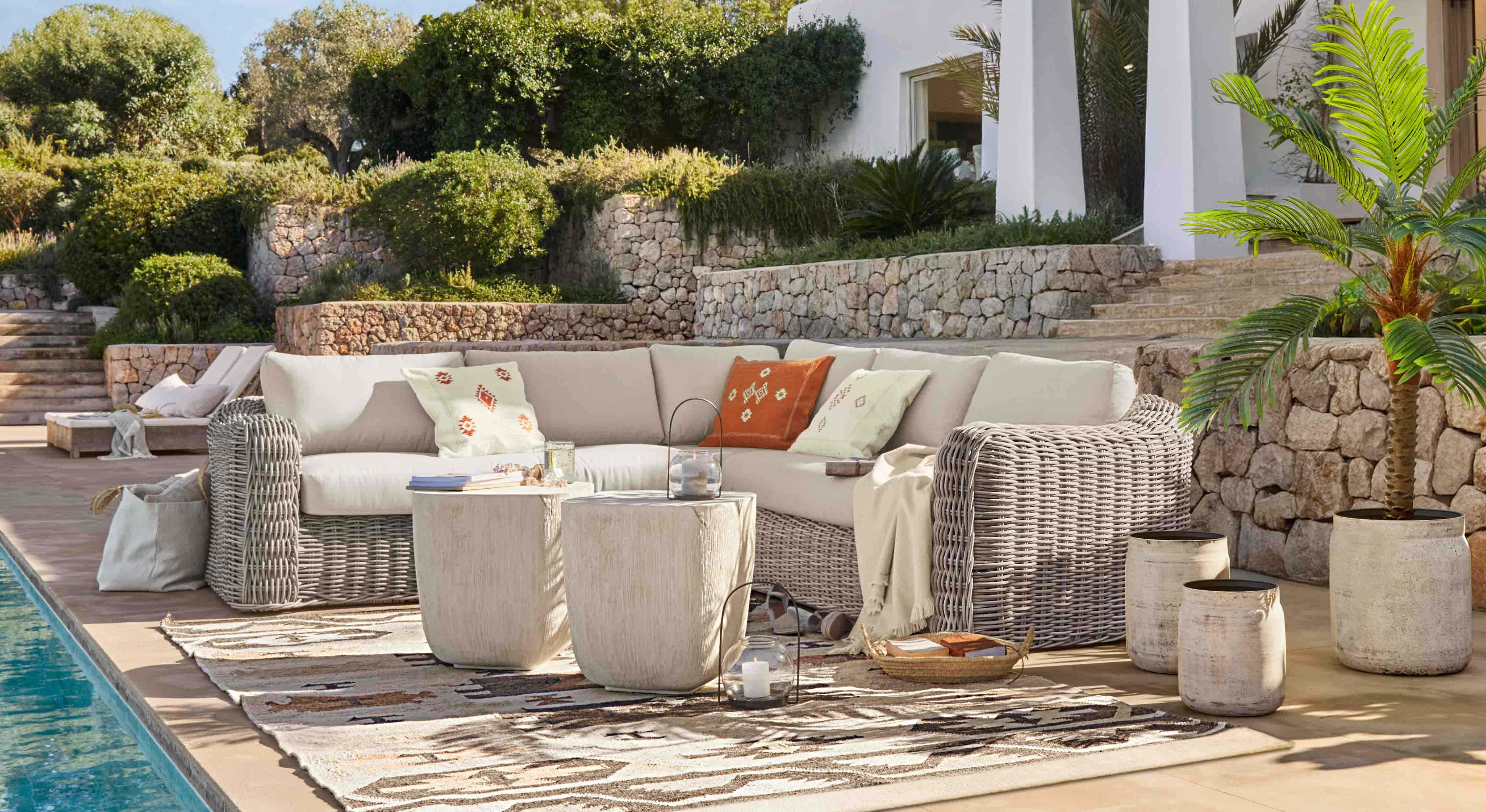 Ensemble de mobilier de jardin en rotin gris clair avec coussins crème et coussins décoratifs sur terrasse au bord de la piscine
