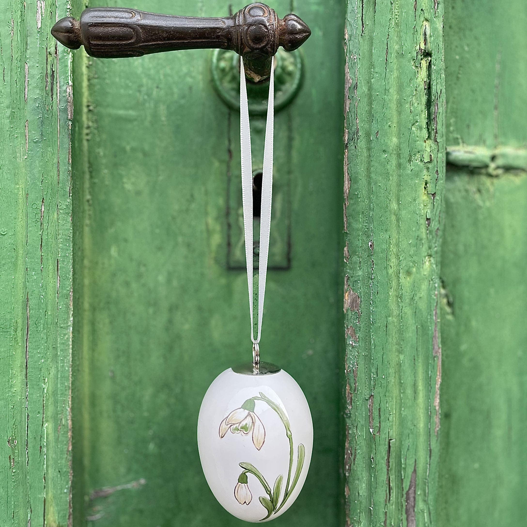 Décoration de Pâques en forme d'œuf en céramique blanche avec motif floral suspendue à une porte verte