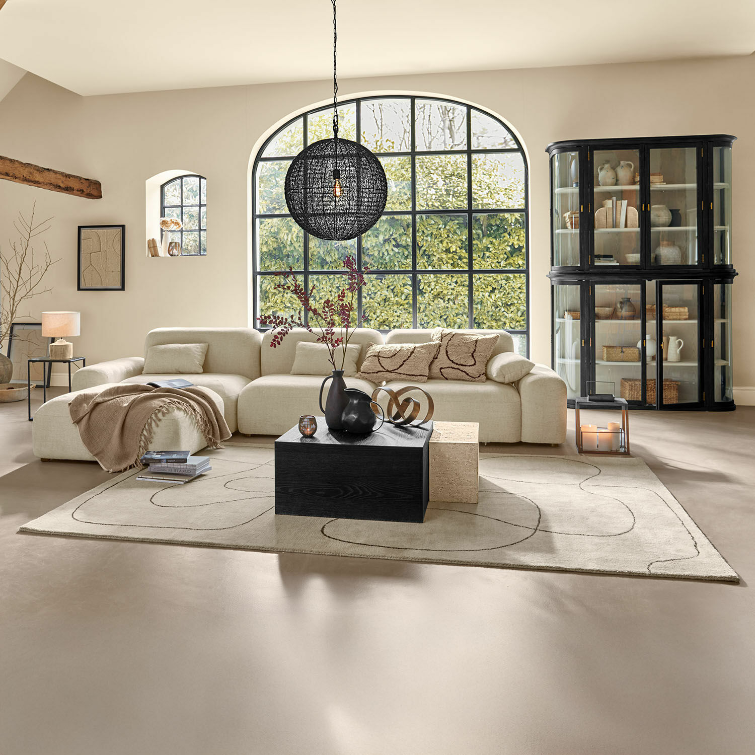 Tapis Lavinois Salon spacieux avec canapé beige en tissu, table basse noire en bois et grande fenêtre donnant sur la verdure