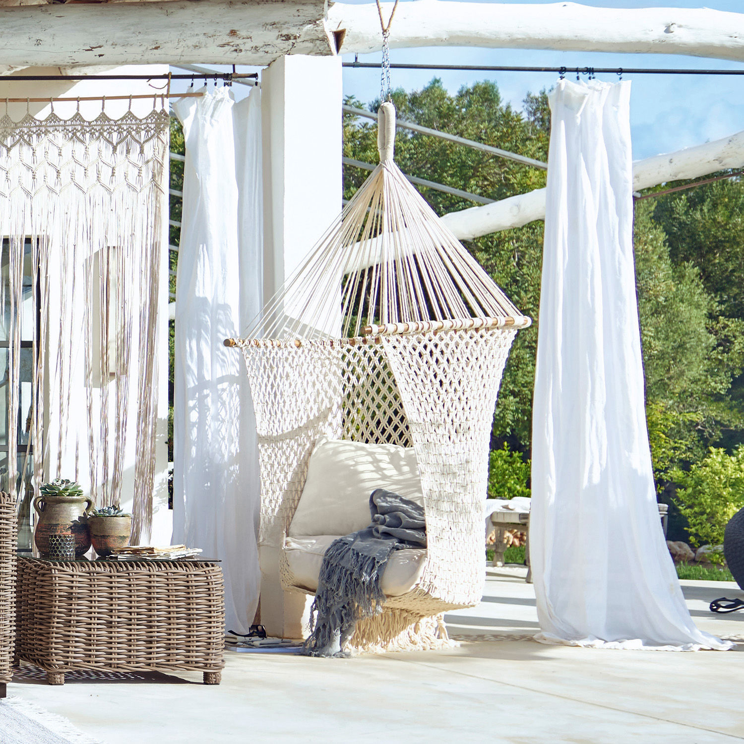 Fauteuil à suspendre Raffaelle Fauteuil suspendu en corde de coton tressée crème avec coussin sur terrasse lumineuse extérieure