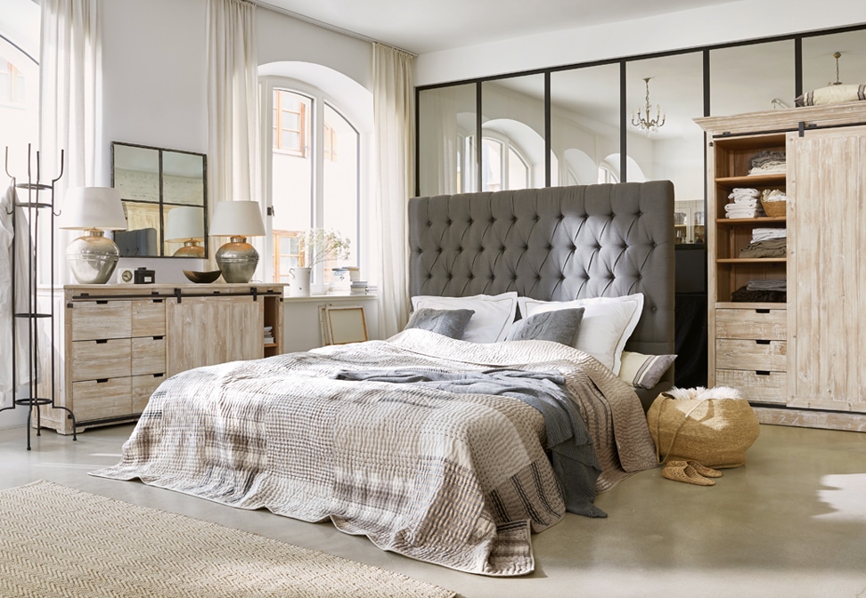 Chambre chaleureuse avec lit à tête capitonnée grise et meubles en bois style loft lumineux