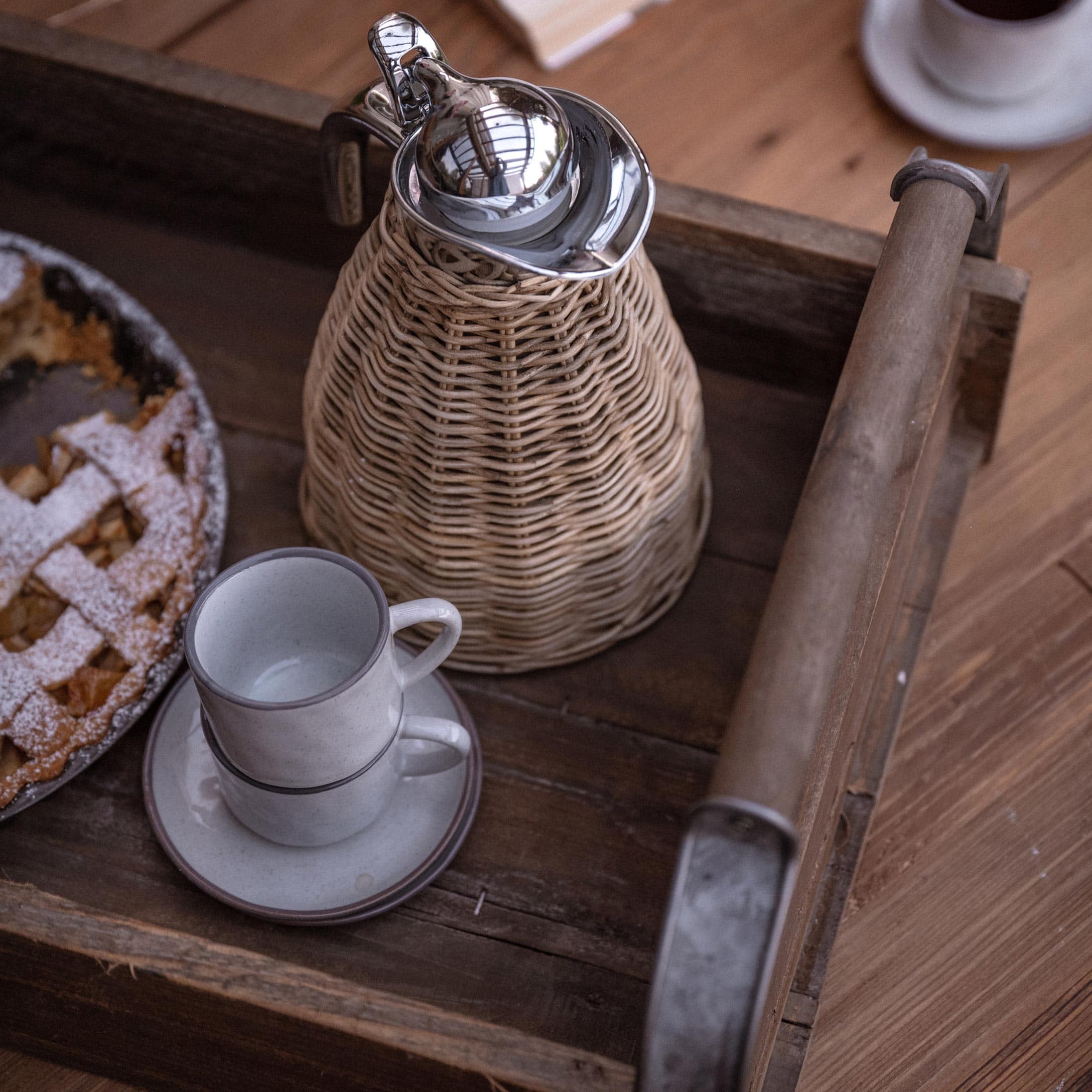 Plateau rustique en bois avec pichet en rotin et deux tasses à café blanches empilées