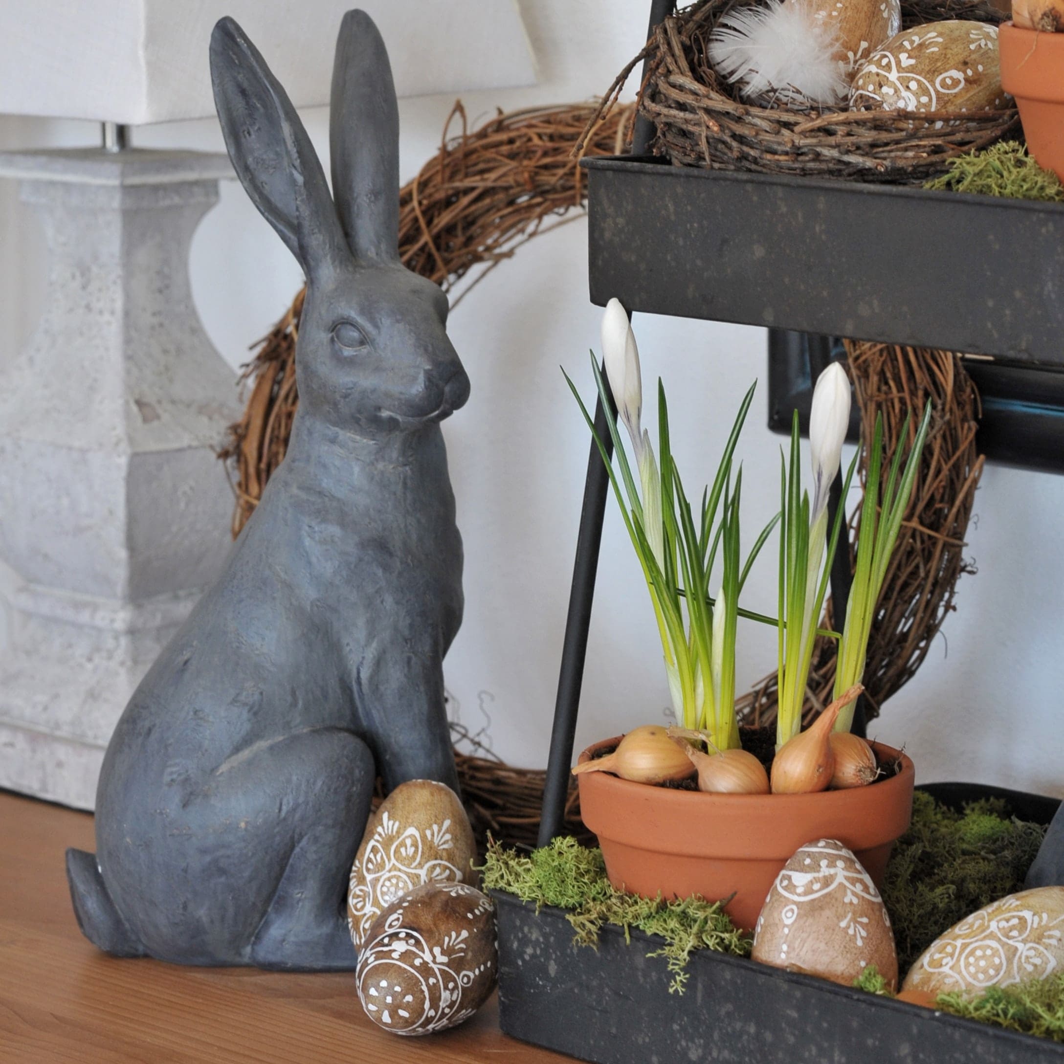 Lapin décoratif gris en céramique à côté d'un pot avec fleurs blanches et œufs décorés pour Pâques