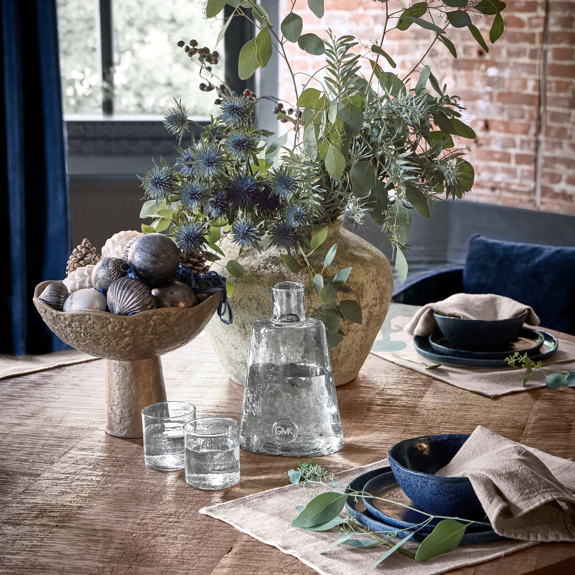 Coupe décorative en métal avec ornements et vase avec feuillage vert sur table en bois dans un salon