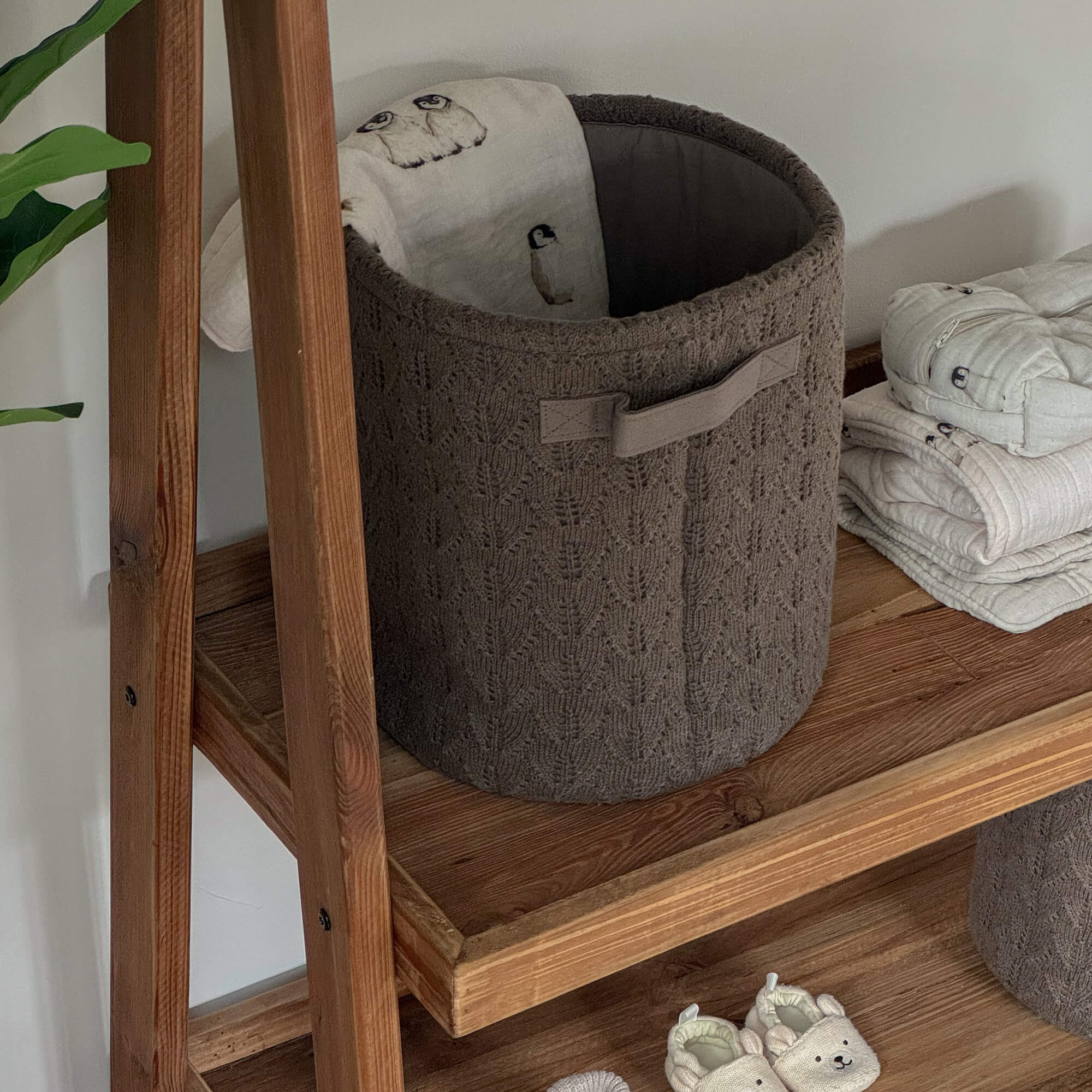 Panier tricoté marron sur étagère en bois avec tissu doux et chaussons pour bébé beige