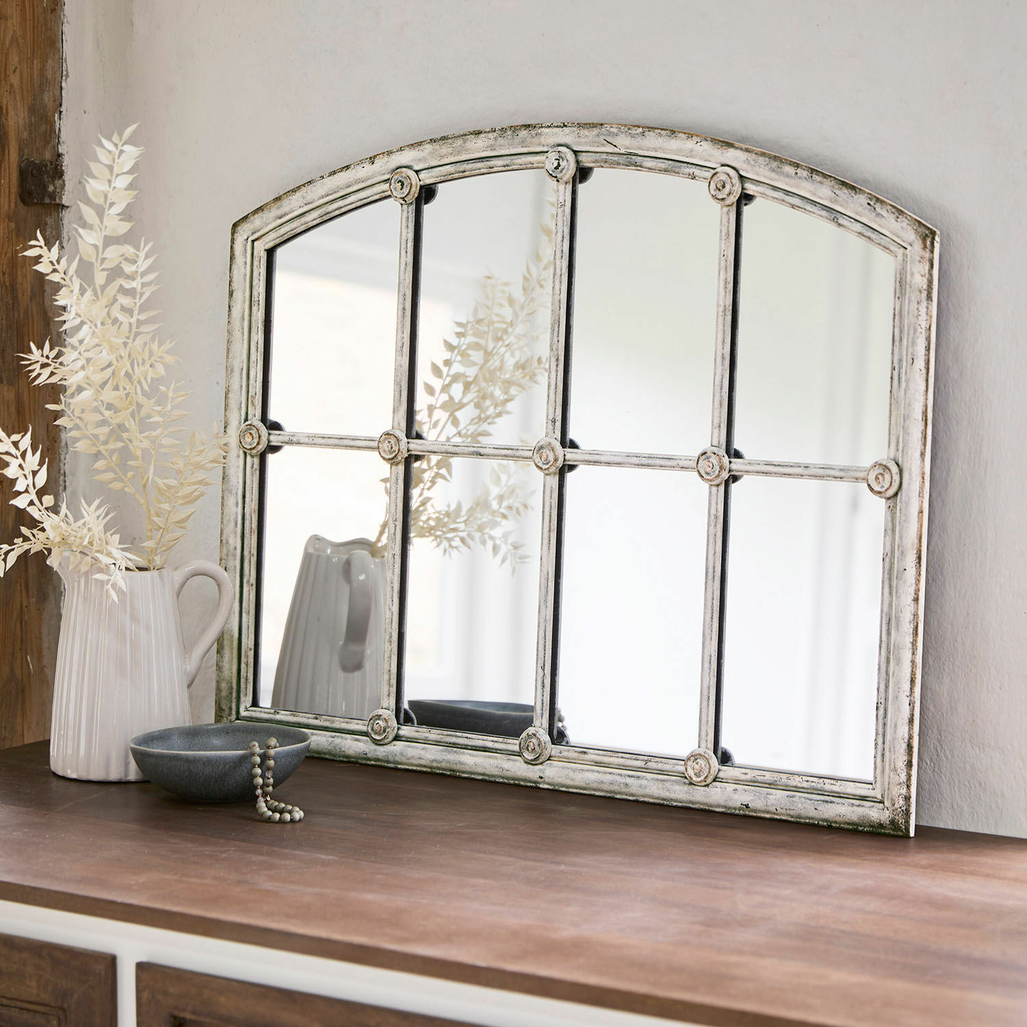 Miroir Tobiah Miroir rustique avec cadre en métal blanc vieilli posé sur un meuble en bois foncé