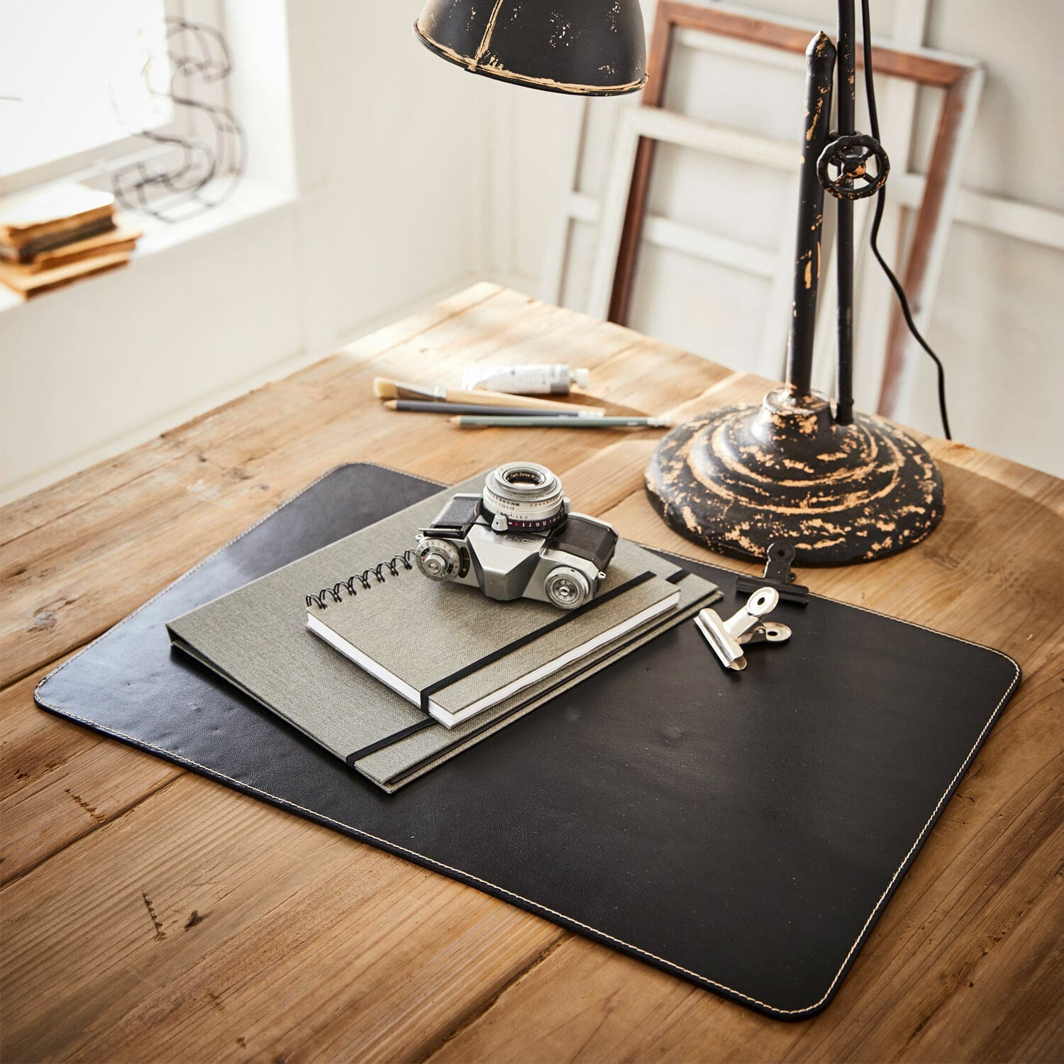 Sous-main Jansen Sous-main en cuir noir avec carnets et appareil photo vintage sur une table en bois clair