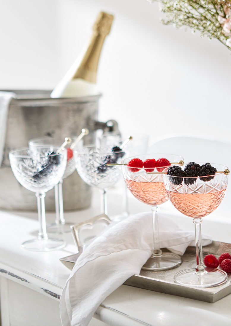 Verres en cristal avec boisson rosée et fruits sur plateau argenté, seau à glace et bouteille en arrière-plan