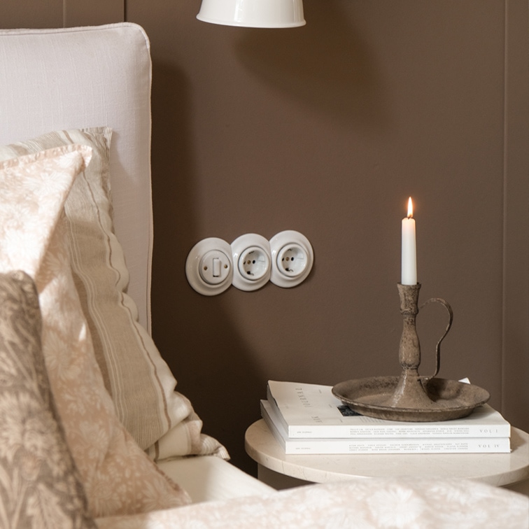 Chandelier en métal rustique avec bougie blanche sur table à côté d'un lit avec literie beige