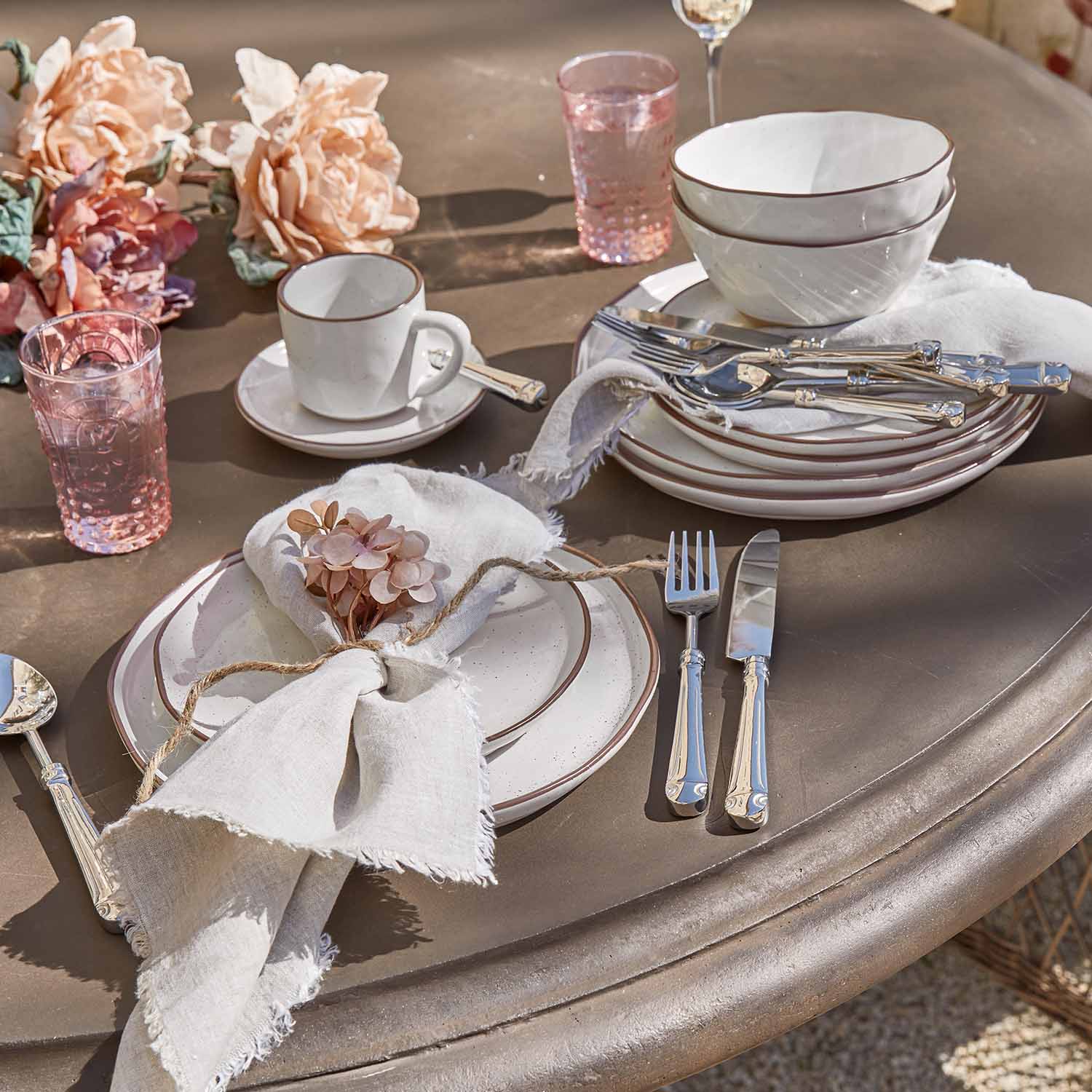 Service de vaisselle en céramique blanche bordée de brun avec verres roses et couverts sur table