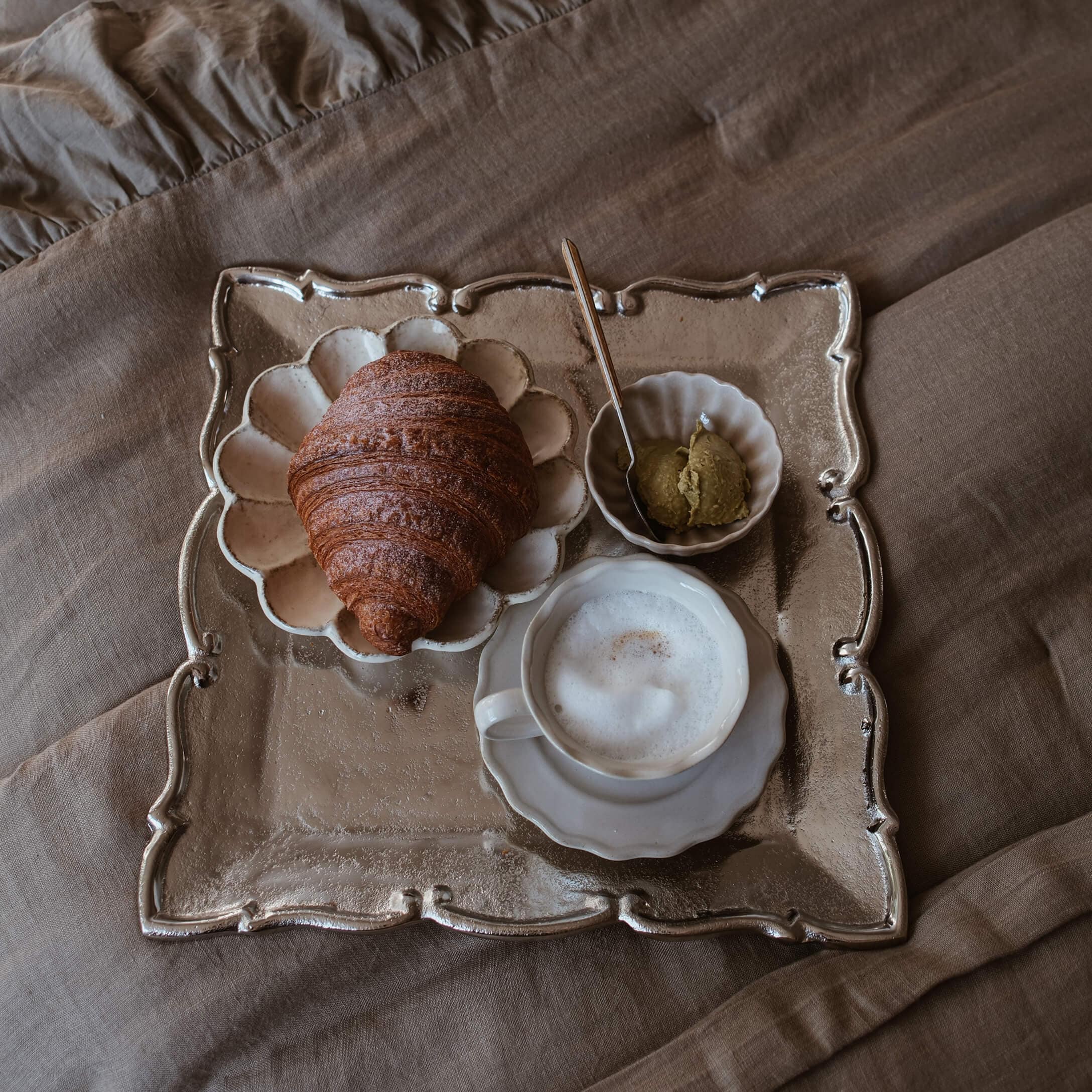 Plateau avec croissant, café mousseux et pâte sur tissu beige, ambiance slow living