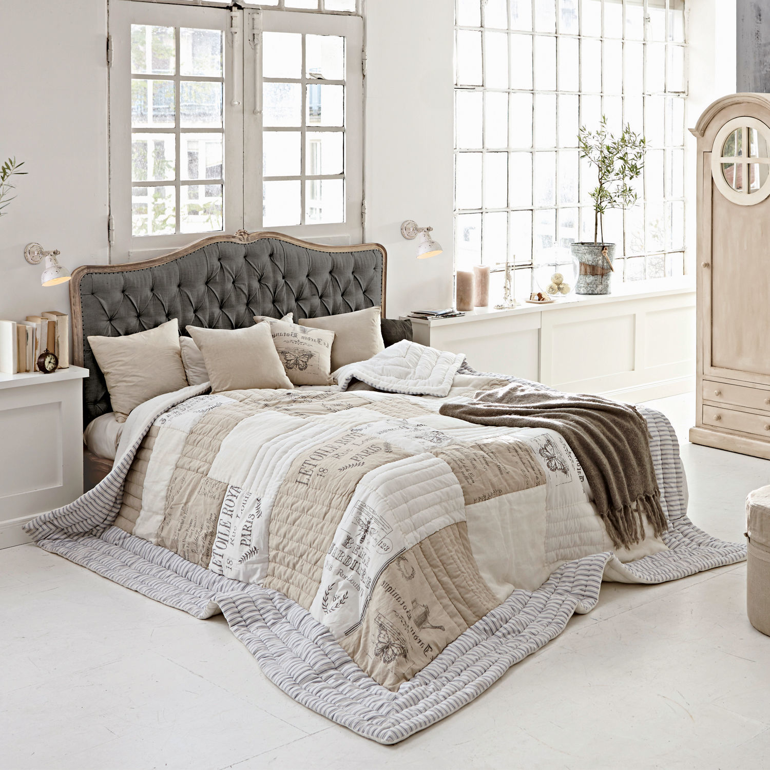 Lit Declaire Chambre chaleureuse avec lit à tête de lit capitonnée grise et couvre-lit beige et blanc à motifs vintage