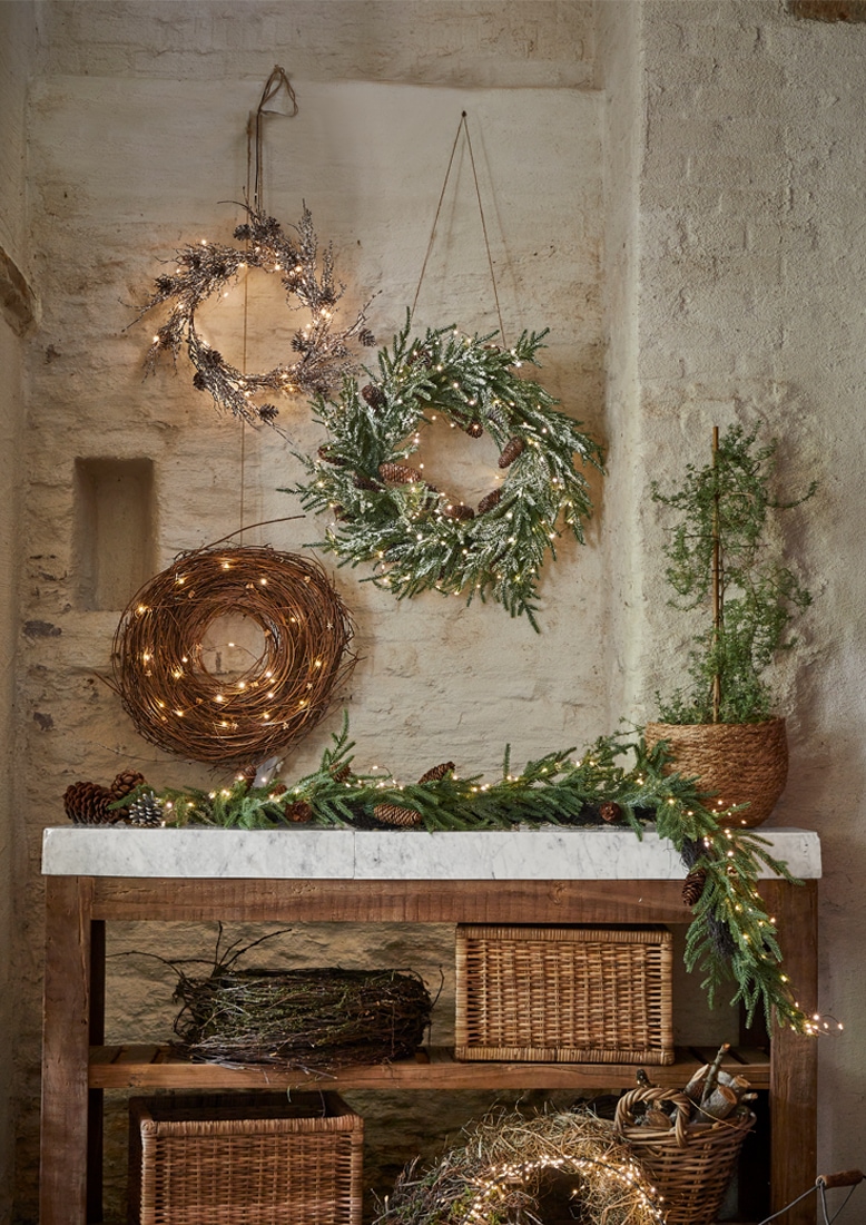 Couronnes décoratives de Noël en branches et lumières suspendues sur mur en pierre et table en bois