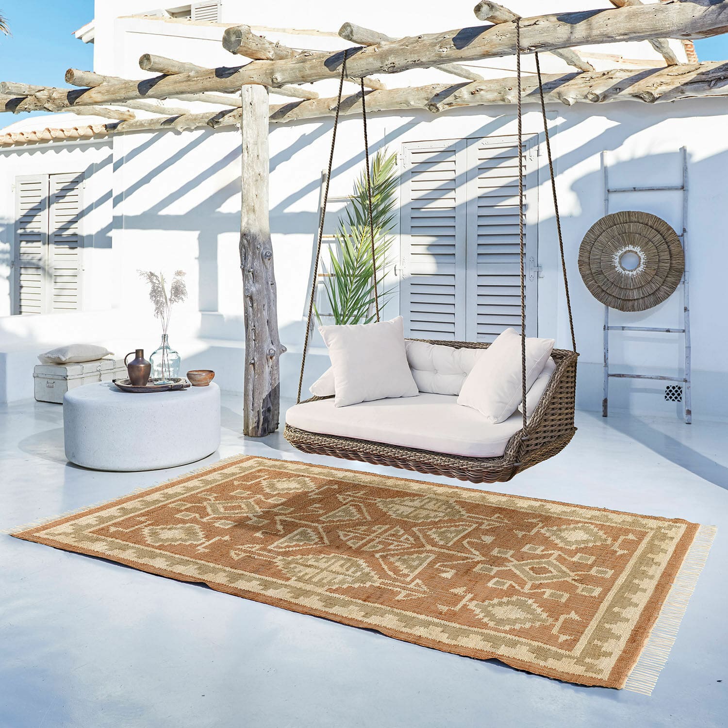 Tapis Serenath Tapis marron et beige à motifs géométriques sur terrasse claire avec balançoire en osier et coussins