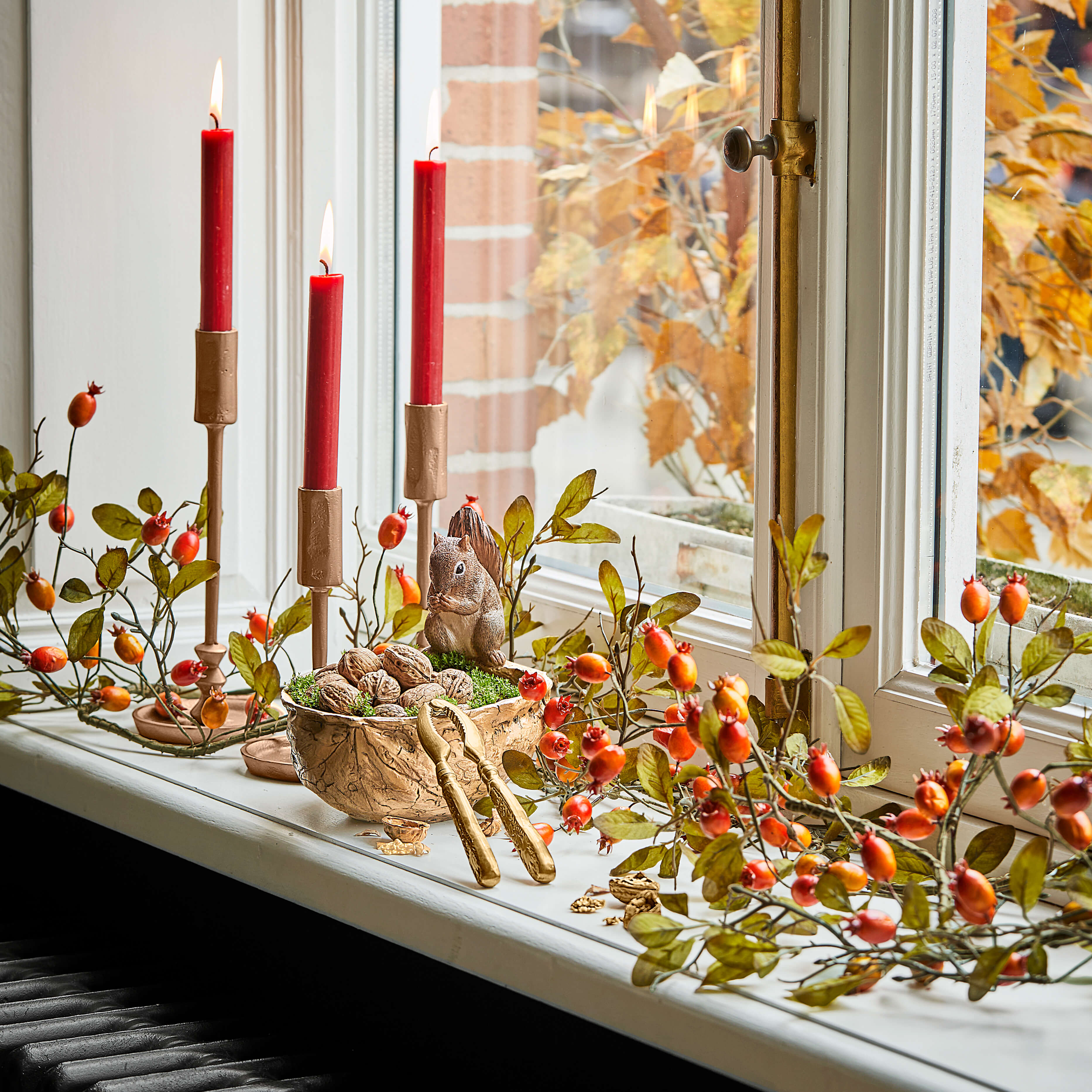Décoration de fenêtre avec bougies rouges, noix et écureuil en figurine dans une ambiance automnale