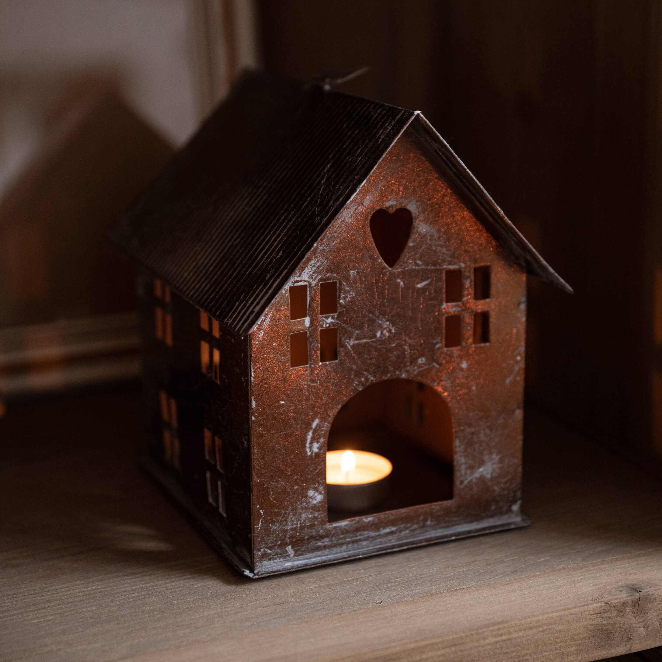 Lanterne en métal en forme de maison avec découpe en cœur et bougie allumée à l'intérieur sur étagère en bois